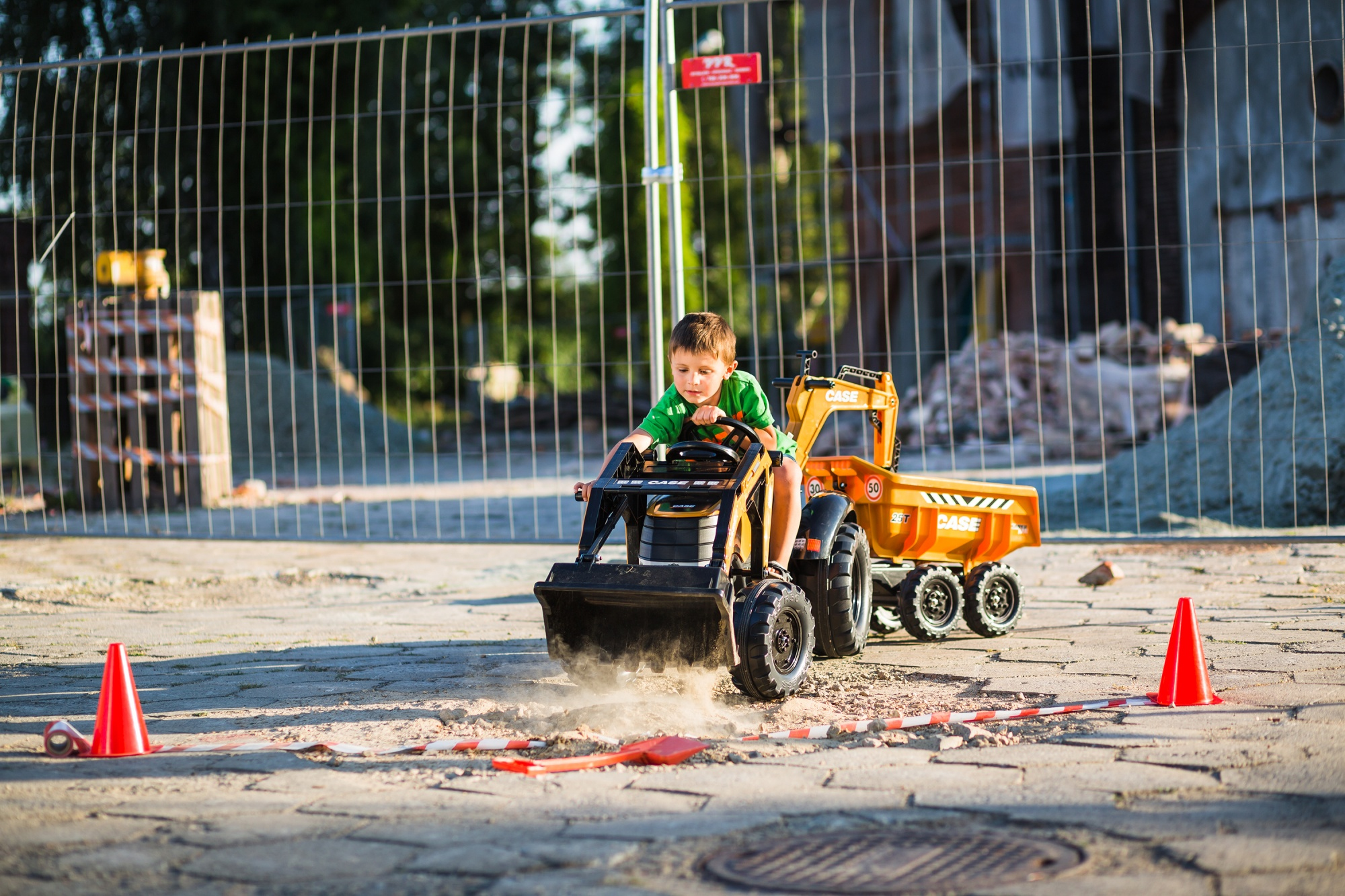 Un ragazzino su un camion giocattolo giallo e nero con un cantiere sullo sfondo.
