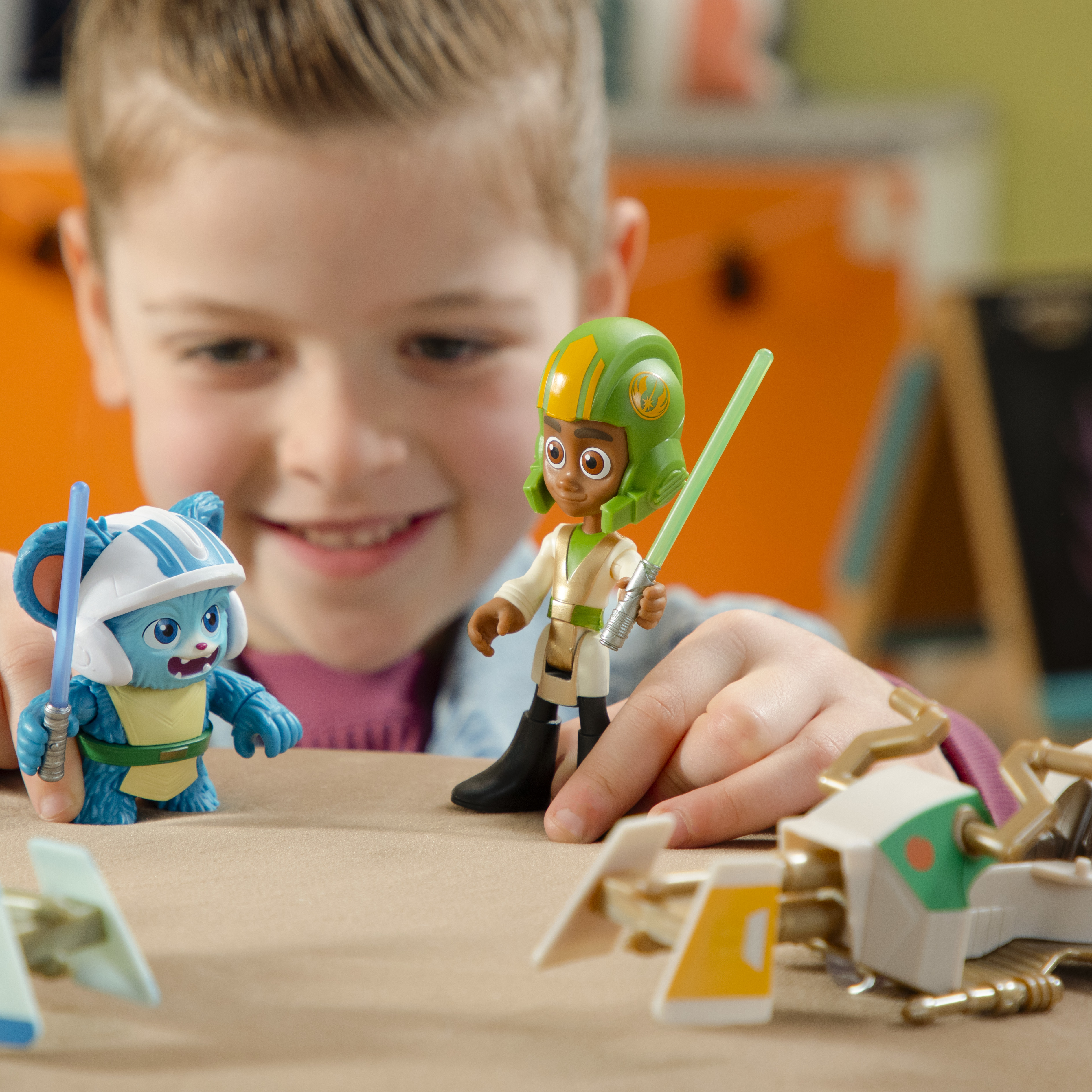 Mała dziewczynka bawi się zabawkami z Gwiezdnych Wojen. Dwie postacie i ścigacze na stole.