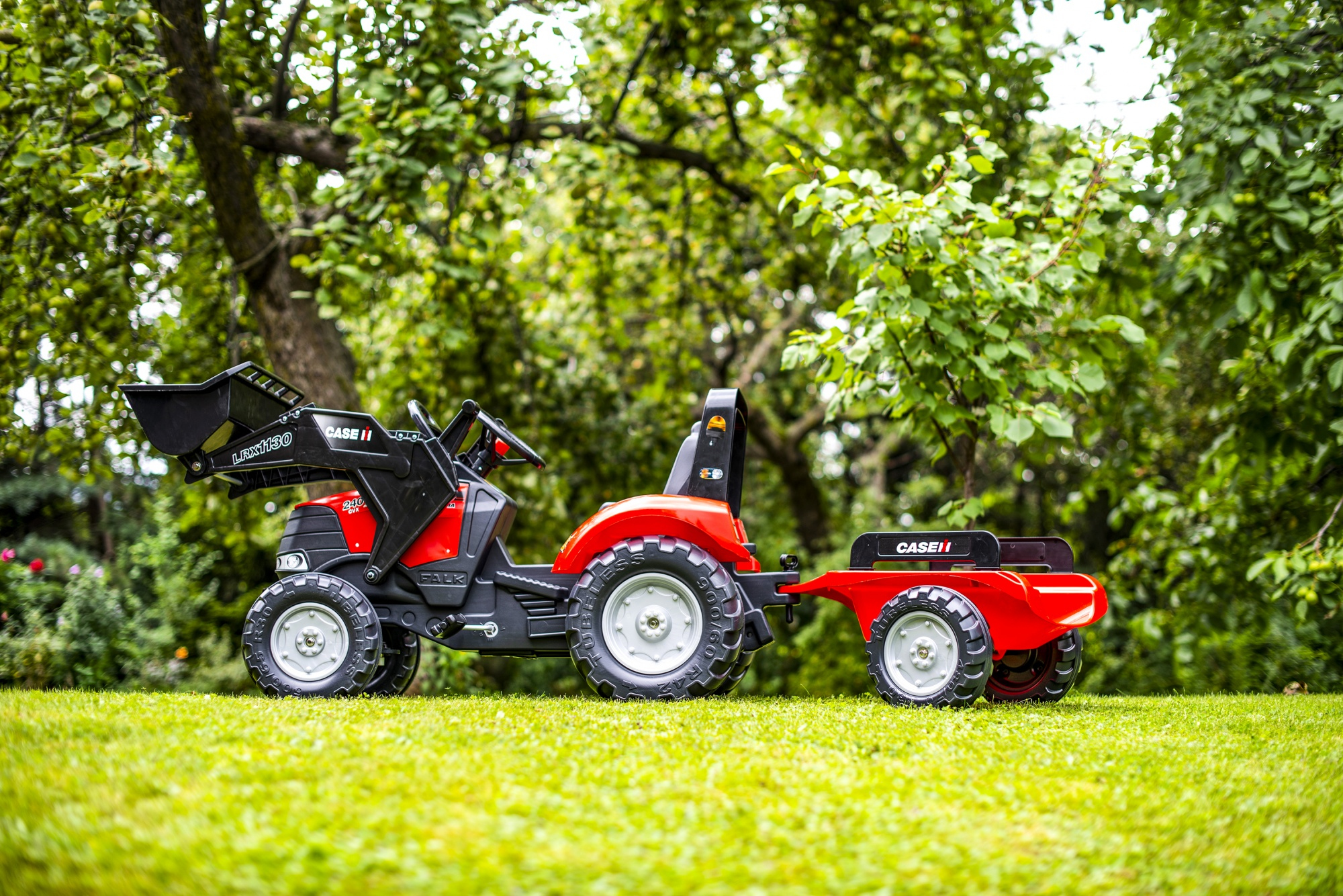 Tractor de juguete rojo con remolque sobre césped verde.