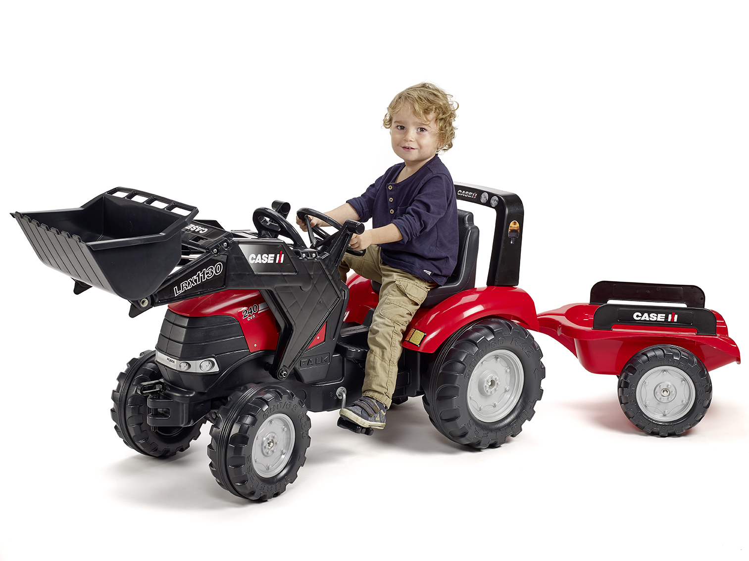 Un niño pequeño sentado en un tractor rojo con remolque, sonriendo a la cámara.