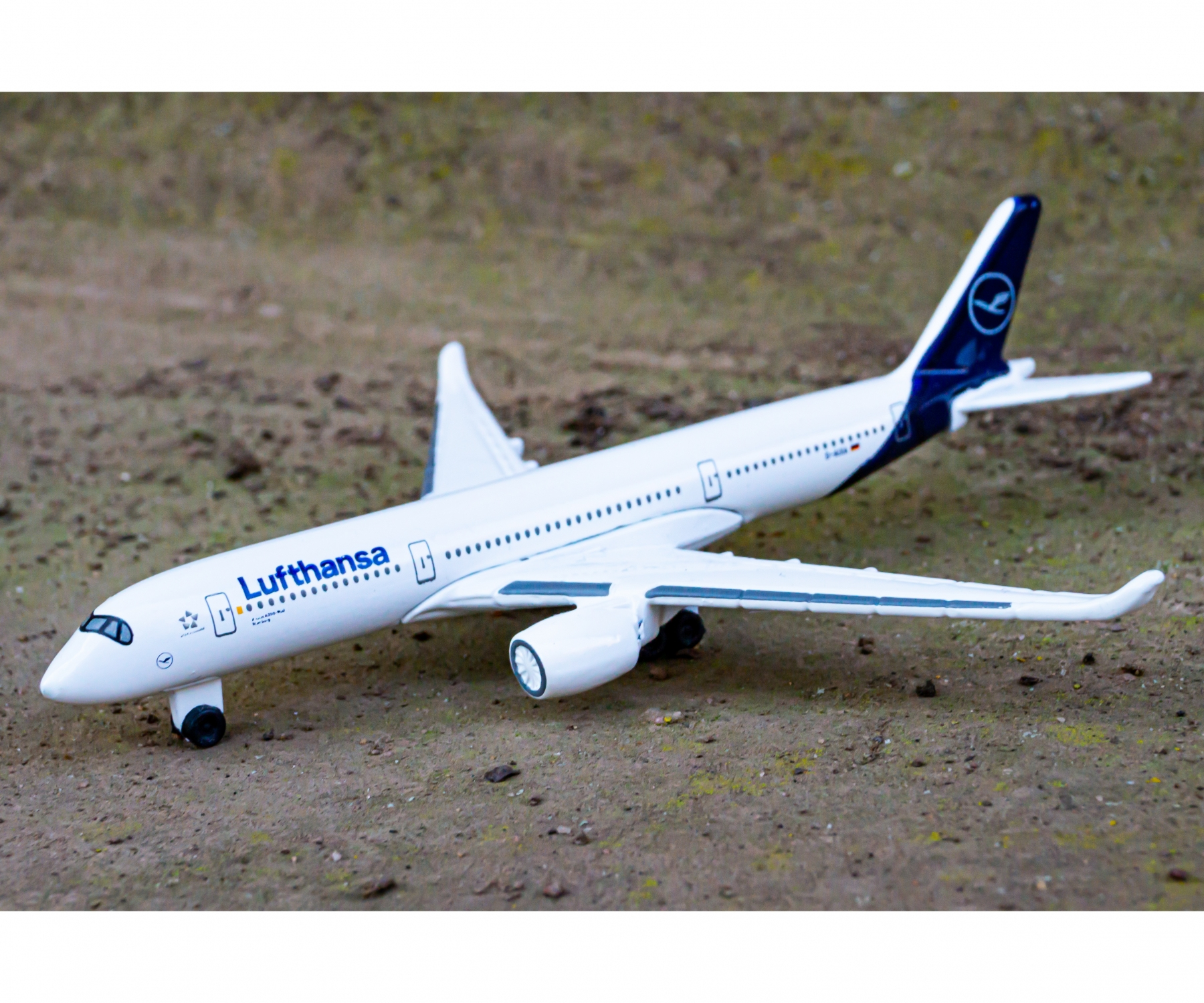 Ein Lufthansa Spielzeugflugzeug auf sandigem Untergrund. Das Flugzeug ist weiß mit blauen Details.