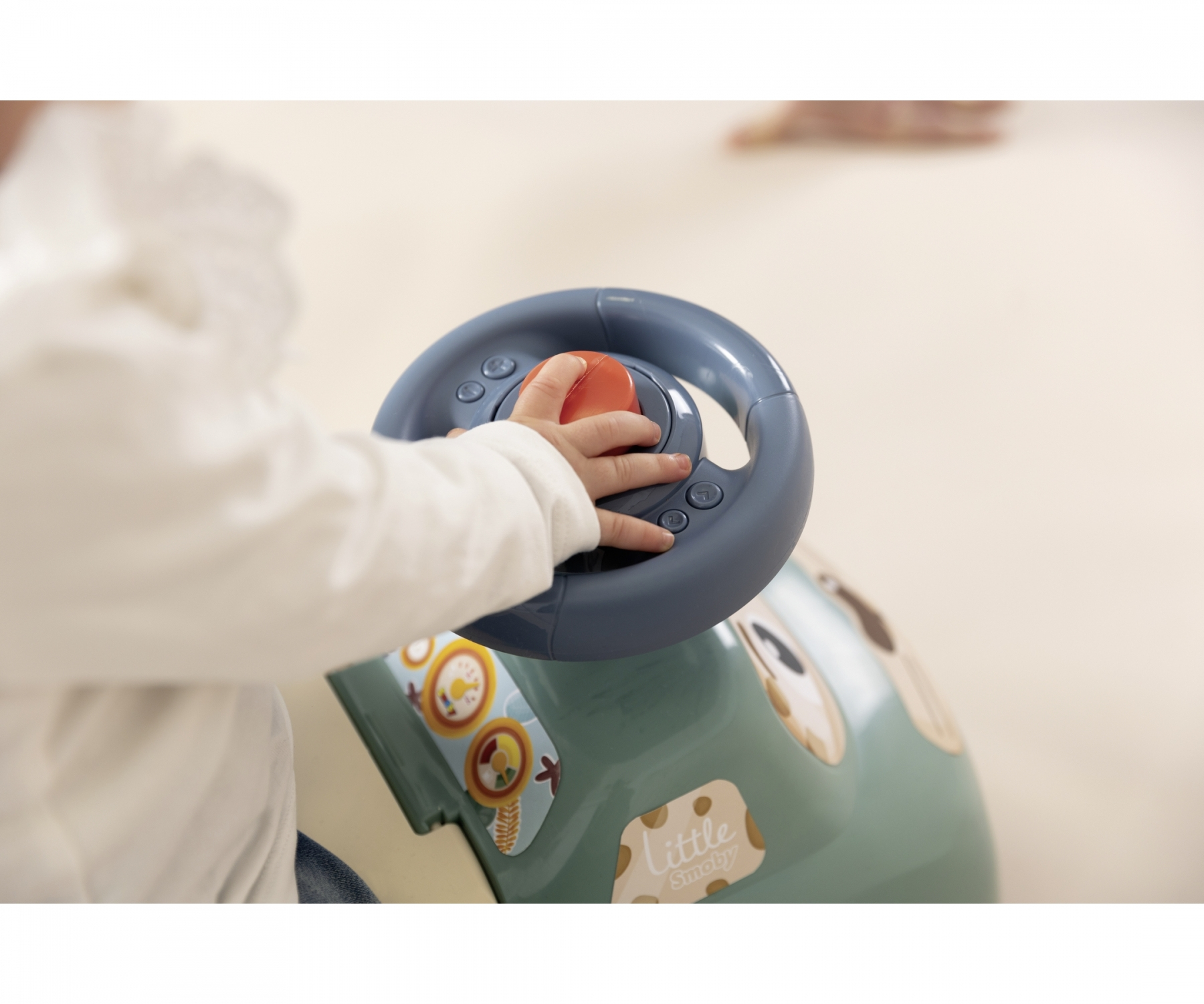Mano di bambino che tiene un volante blu di un'auto giocattolo, primo piano su bianco.
