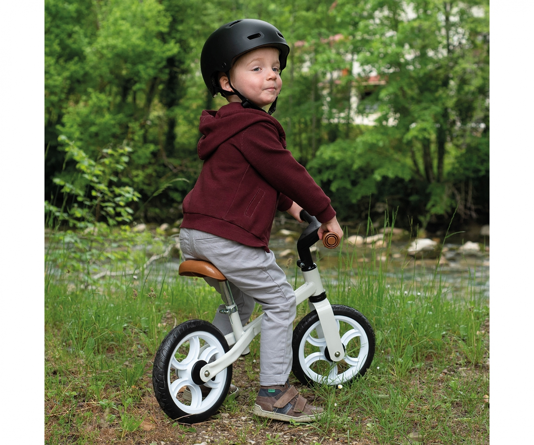 Un bambino con il casco guida una bici senza pedali su una strada. Sfondo verde.