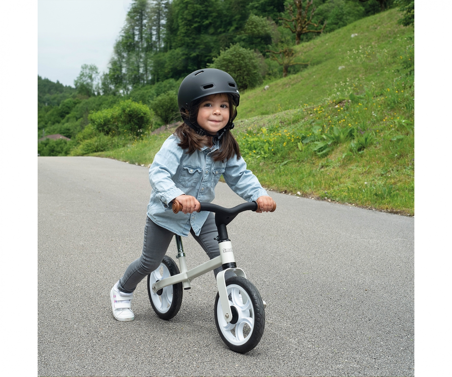 Un bambino guida una bici senza pedali su una strada asfaltata, con un casco. Sfondo verde.