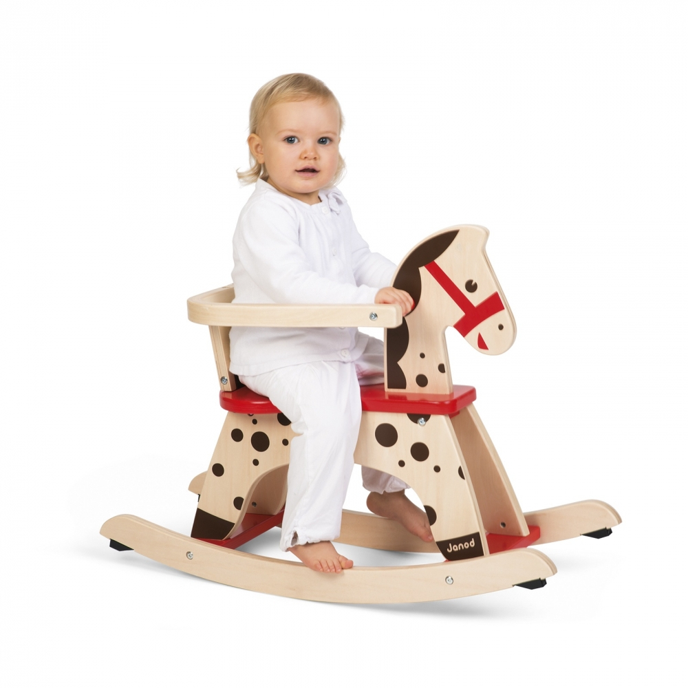 Un bambino piccolo seduto su un cavallo a dondolo in legno, marrone chiaro con dettagli rossi.