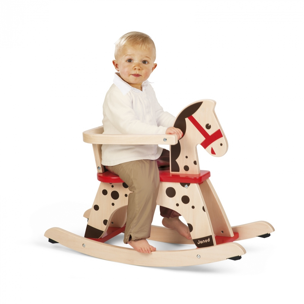 Un bambino piccolo è seduto su un cavallo a dondolo di legno con sedile rosso e macchie nere.