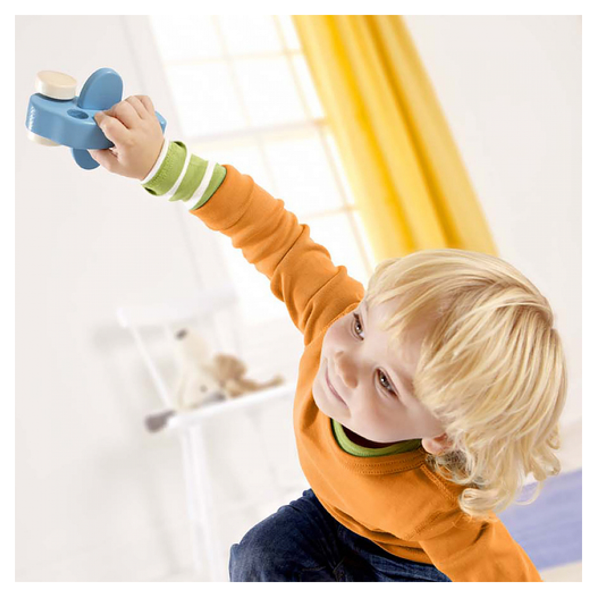 Blond dziecko trzymające niebieski samolot zabawkowy, z rozmytym tłem.