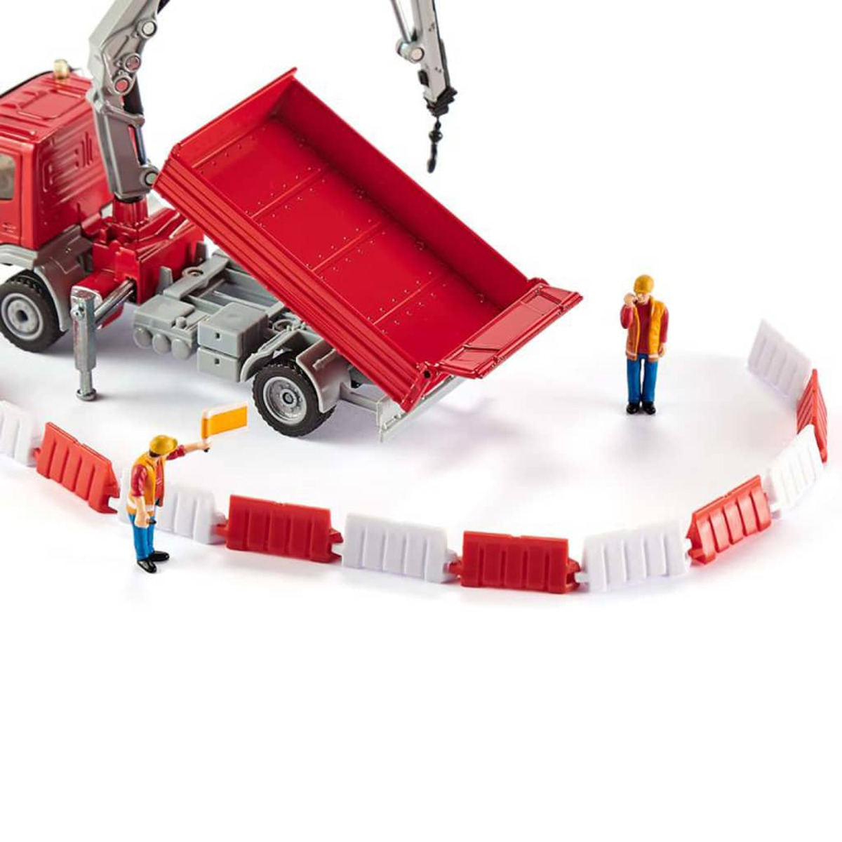 Zabawkowa scena budowy z czerwoną ciężarówką, robotnikami i barierami bezpieczeństwa. Dźwig podnosi skrzynię ładunkową.