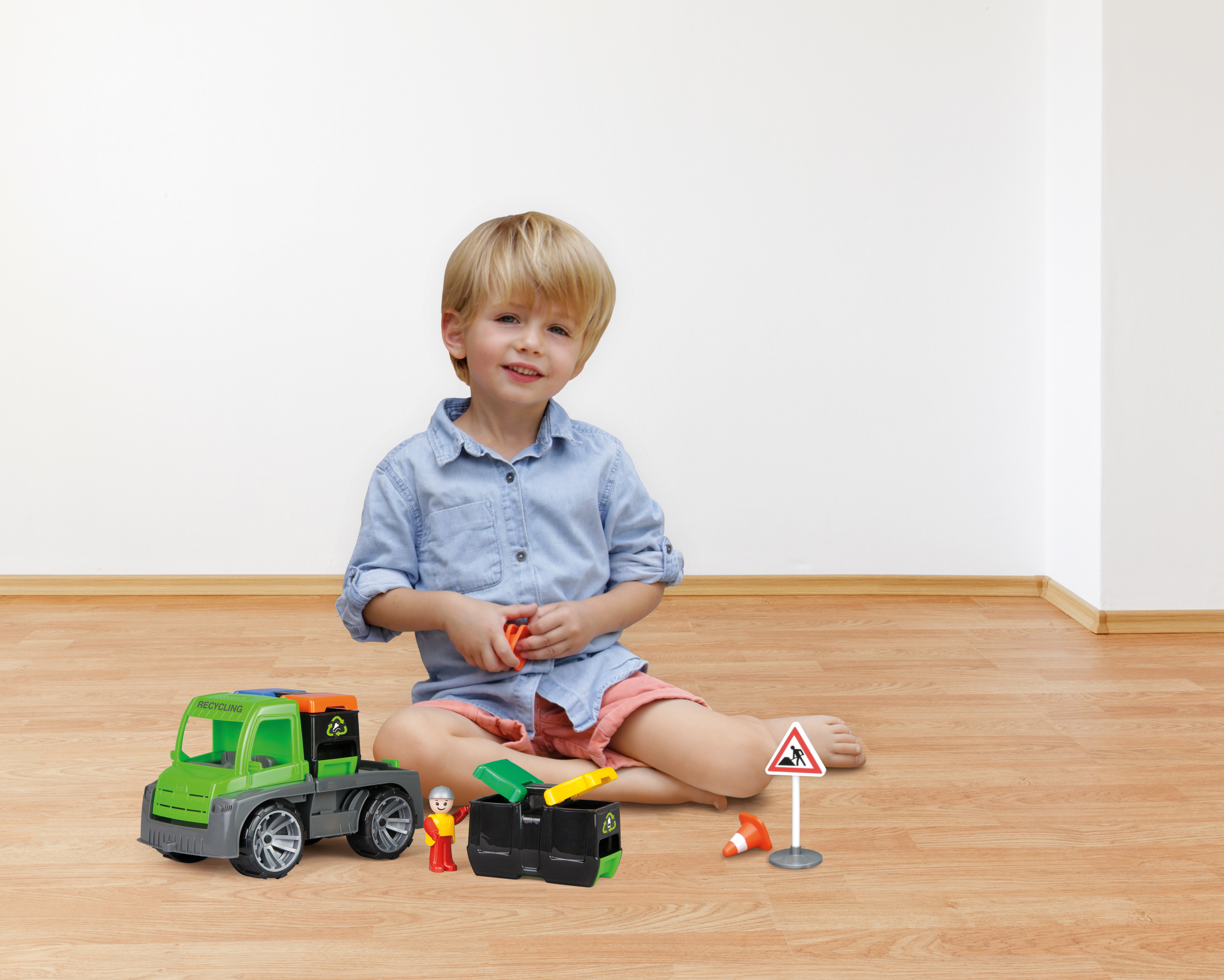 Chłopiec z zabawką recyklingową, znakiem drogowym i pachołkiem na drewnianej podłodze.