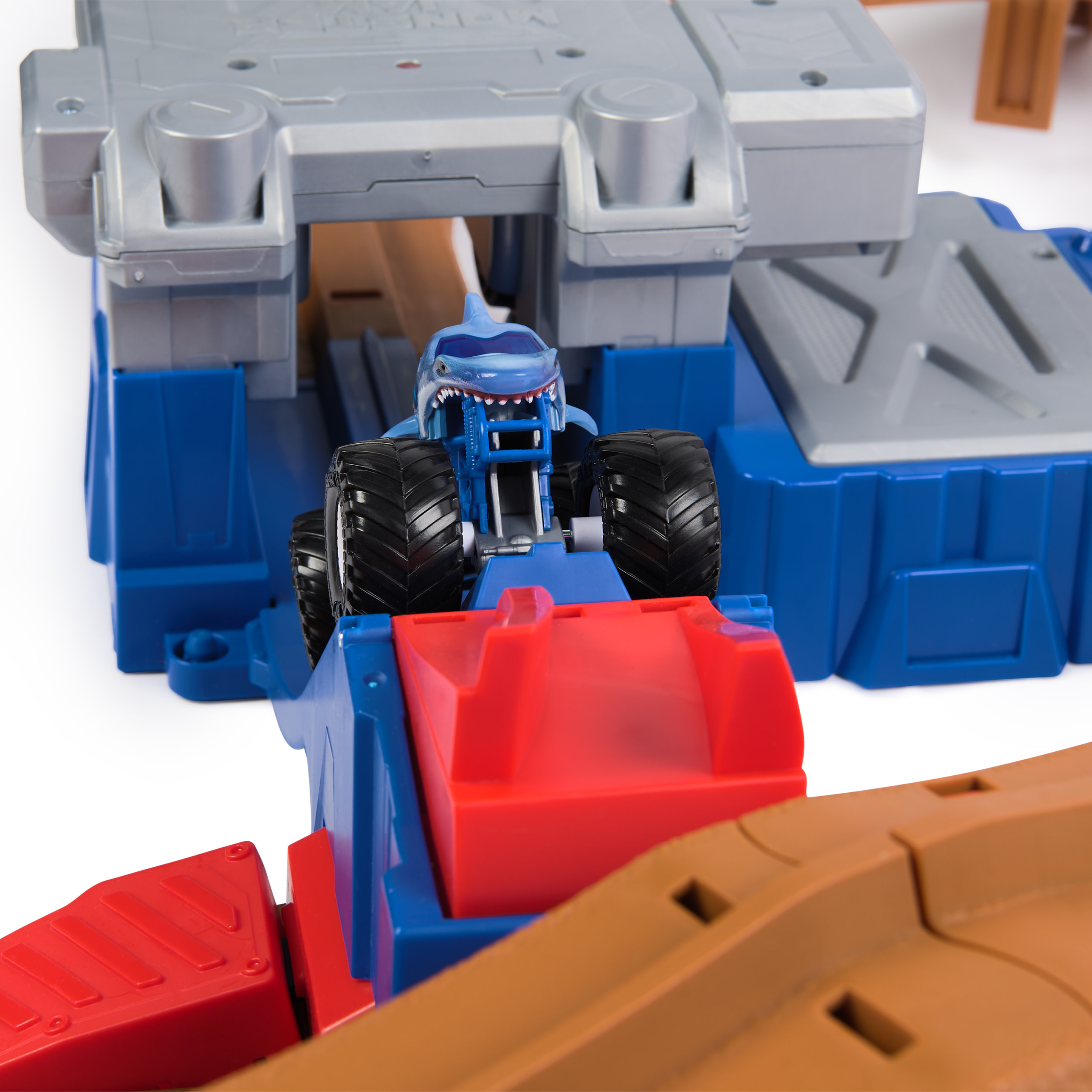Zabawkowy monster truck na torze, z motywem rekina i niebieską konstrukcją.