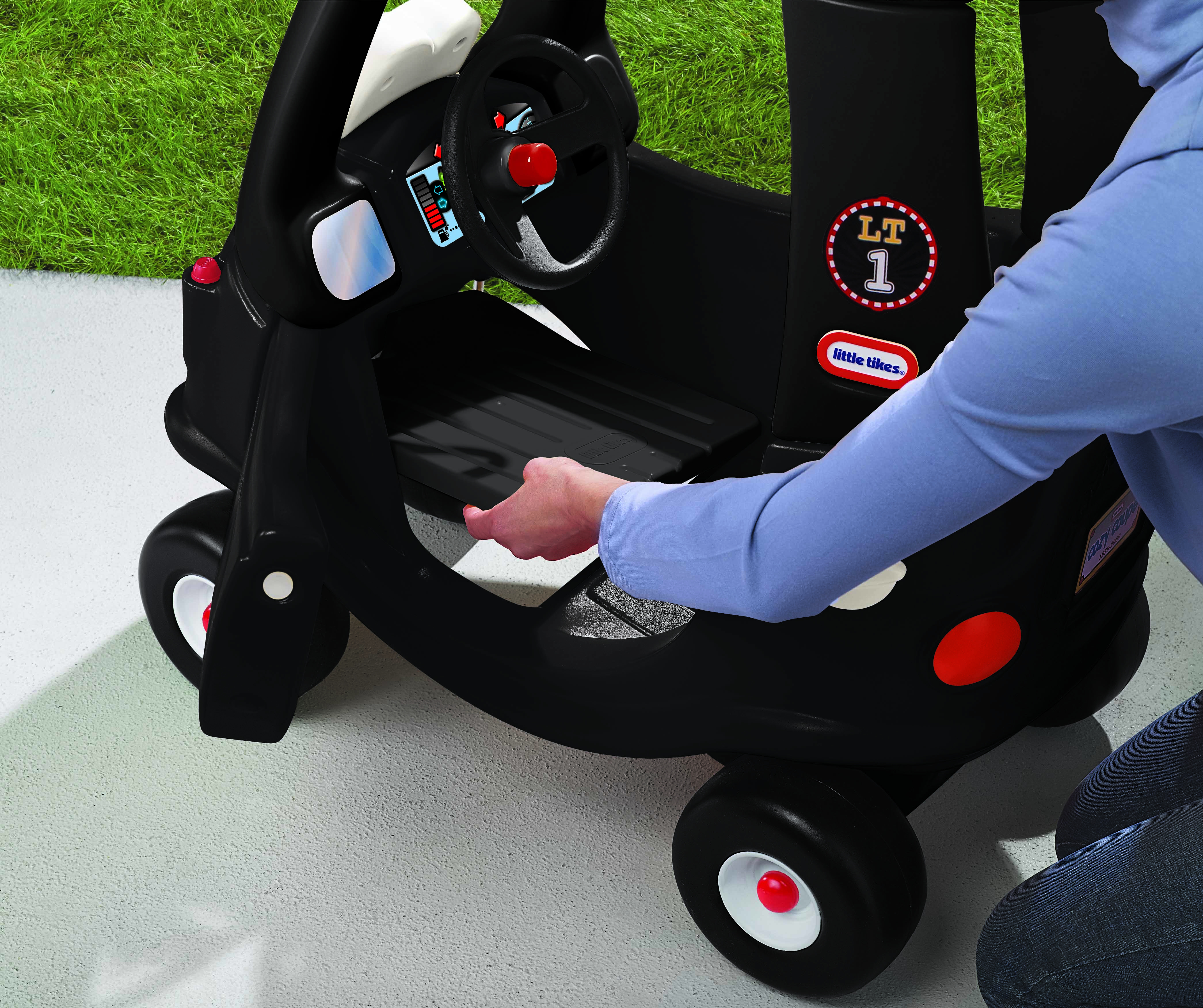 Una persona sta appoggiando a terra un'auto giocattolo Cozy Coupe taxi nera.