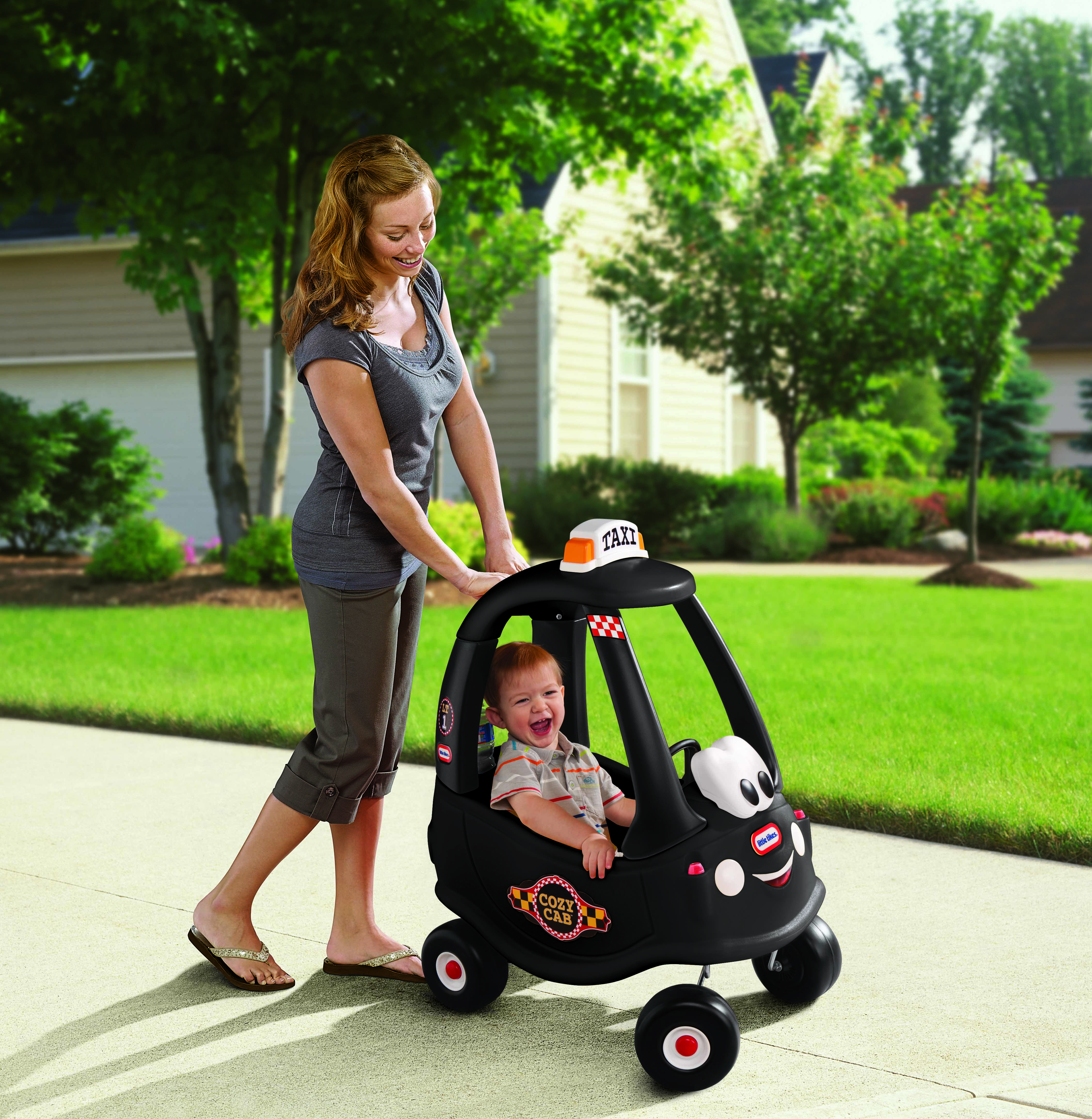 Una donna che spinge un bambino su un'auto giocattolo Cozy Coupe taxi nera su un marciapiede.