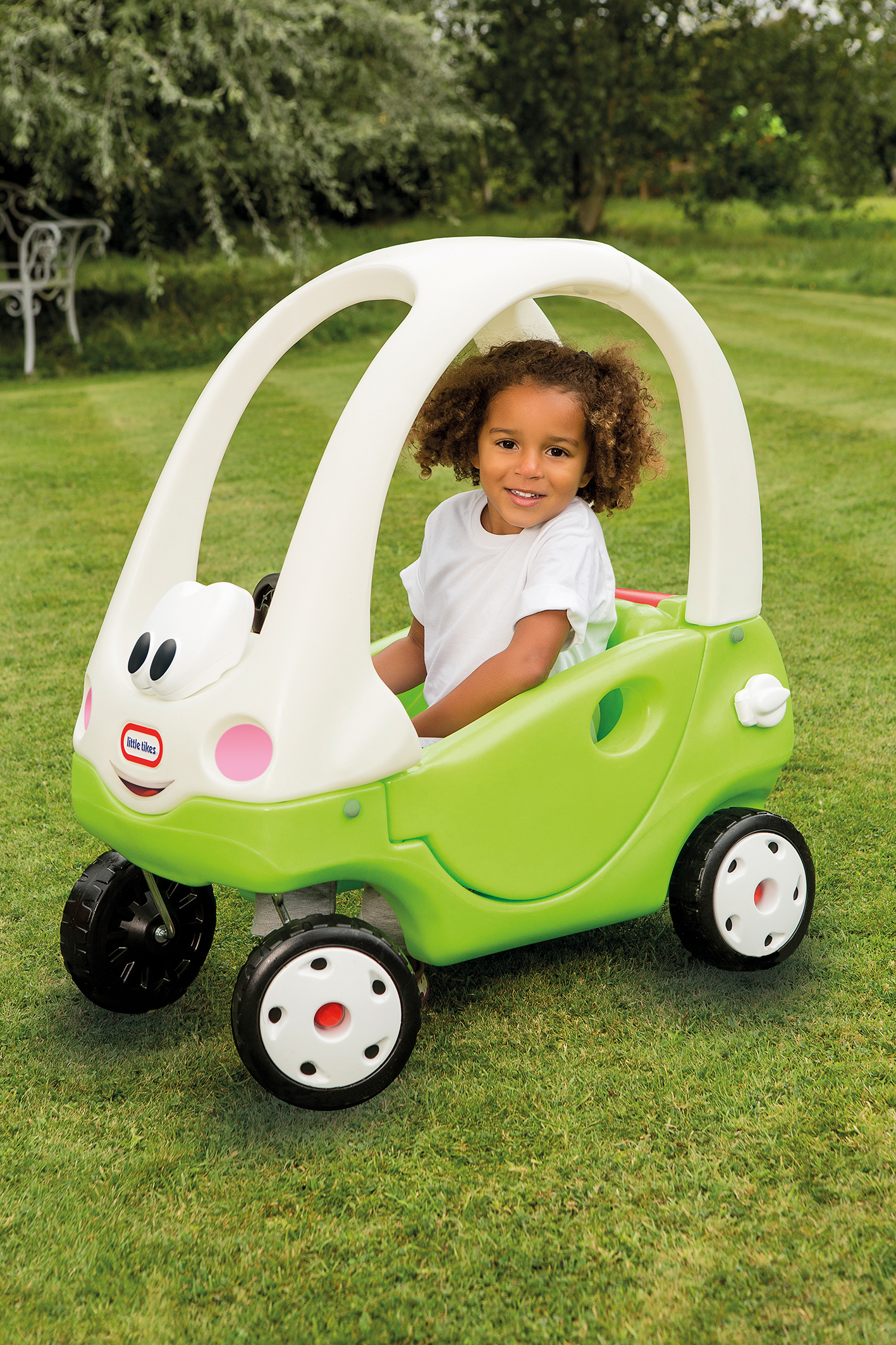 Una bambina è seduta in un'auto giocattolo verde e bianca su un prato, sorridendo alla fotocamera.