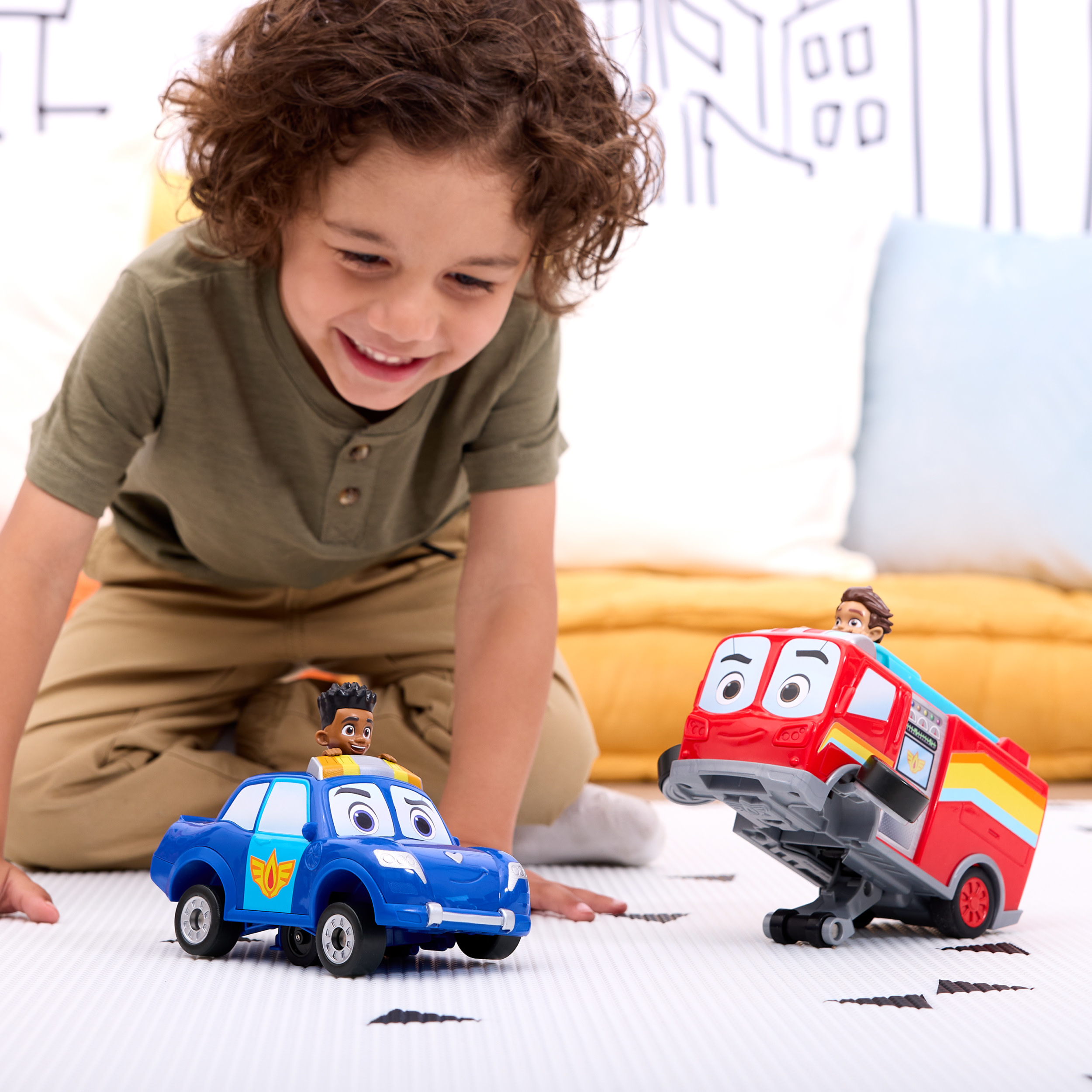 Chłopiec uśmiecha się do dwóch samochodzików, niebieskiego radiowozu i czerwonego wozu strażackiego.