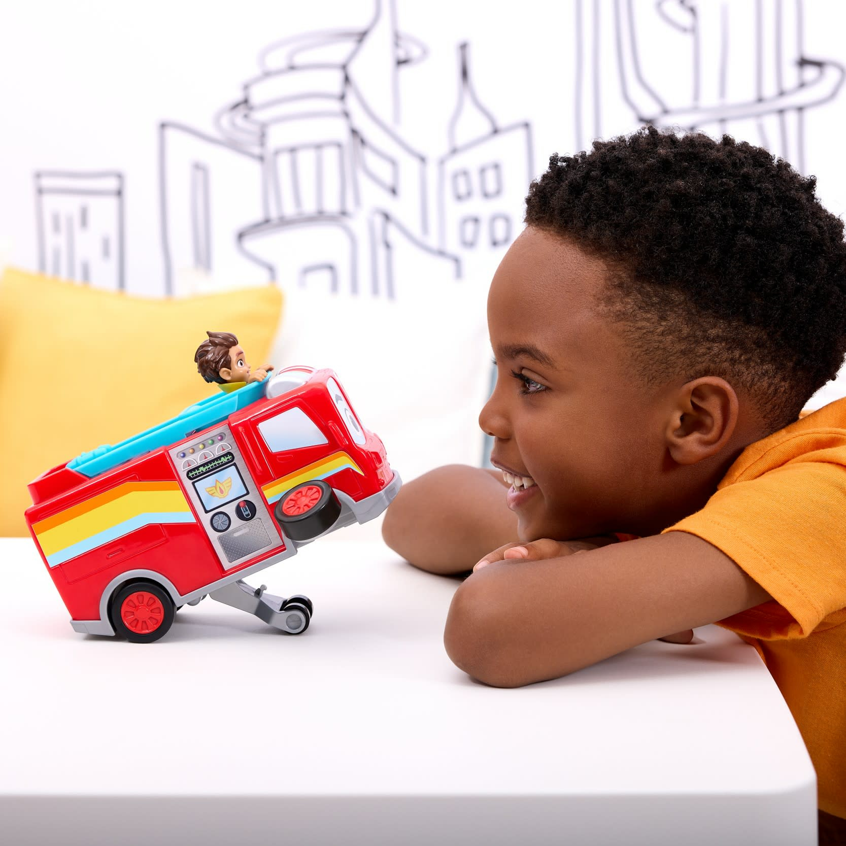 Chłopiec patrzy na czerwoną zabawkę wóz strażacki z figurką strażaka. Ciężarówka stoi na białej powierzchni.