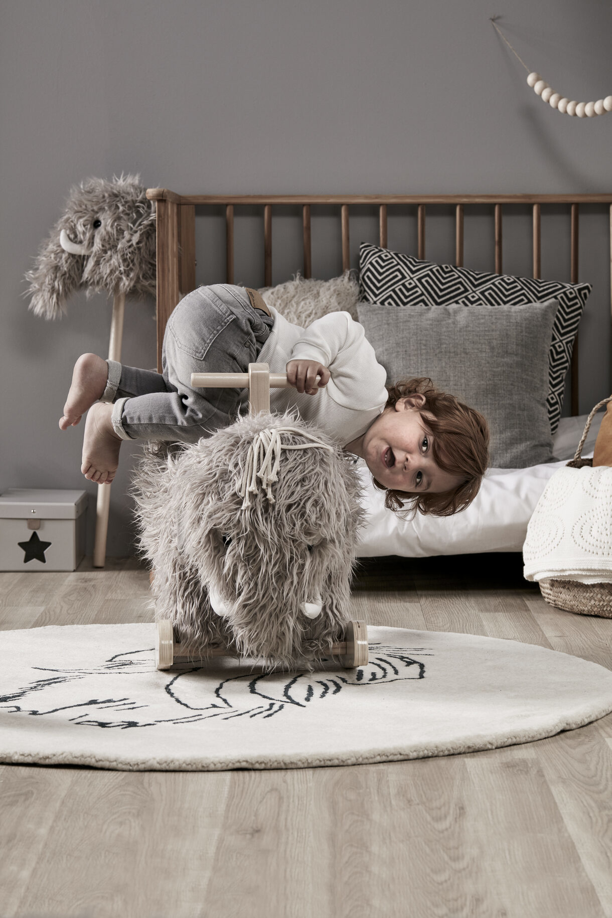 Kind reitet Schaukelpferd in einem Schlafzimmer. Graue Wände und Holzboden.