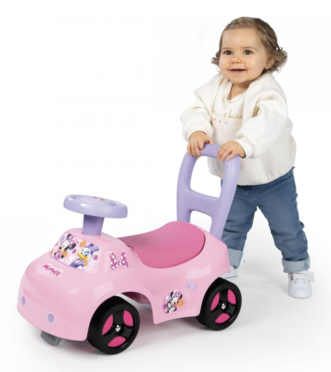 Kleines Mädchen schiebt ein rosa Spielzeugauto mit Minnie Mouse Design, weißer Hintergrund.