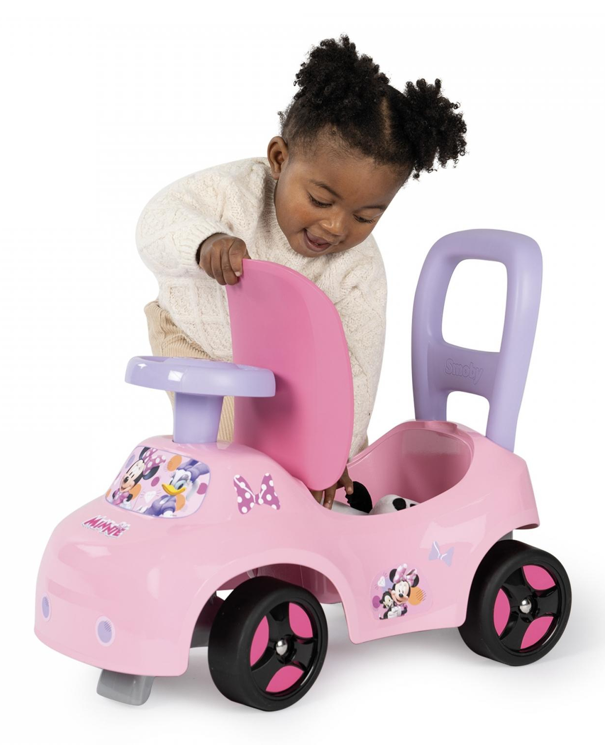 Ein Baby legt eine Puppe in ein rosa Spielzeugauto. Weißer Hintergrund.