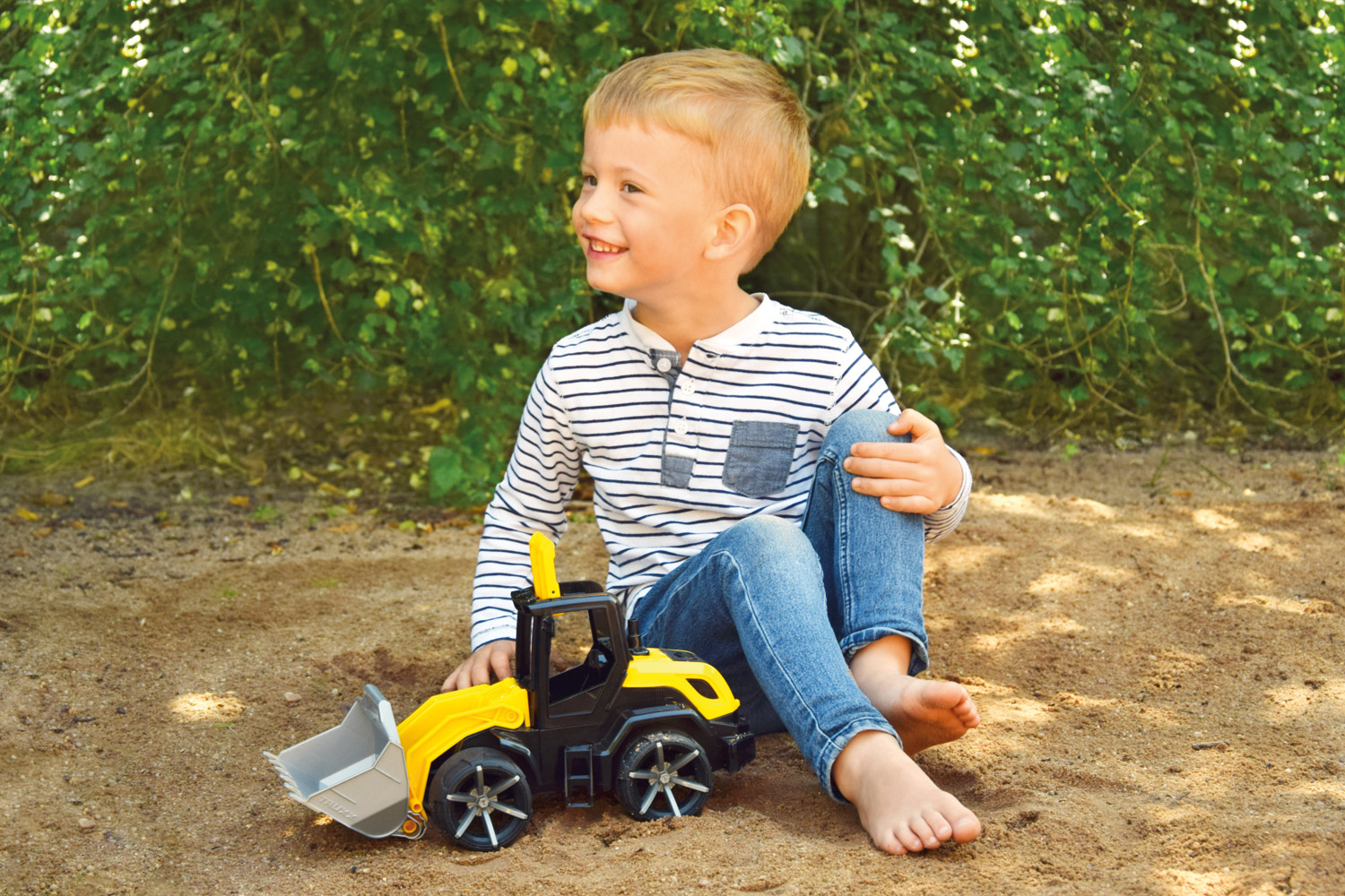 Mały chłopiec uśmiecha się, siedząc obok żółto-czarnej zabawki-ciężarówki.