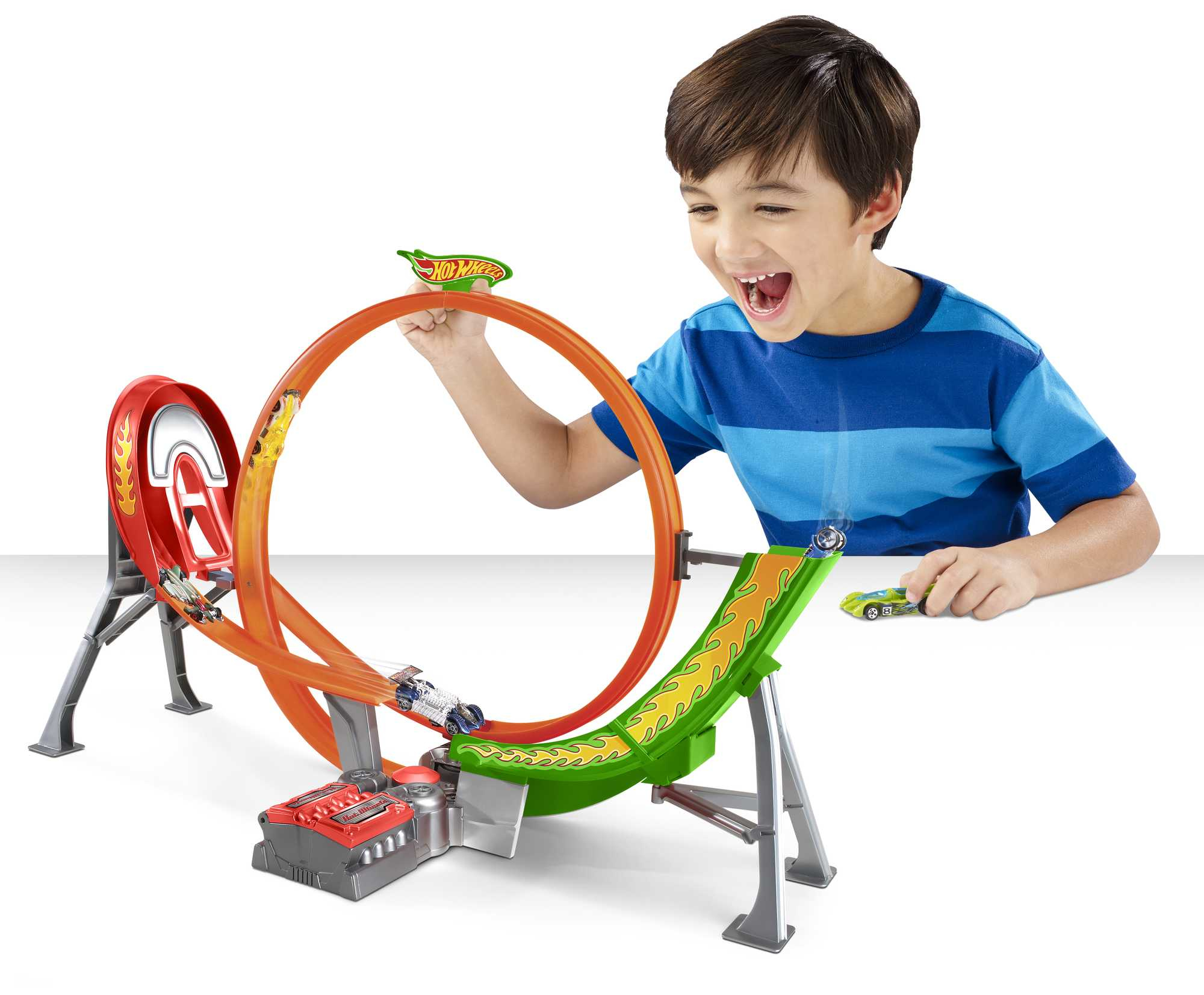 Młody chłopiec bawiący się zestawem torów Hot Wheels, samochody ścigają się na pomarańczowej pętli. Białe tło.