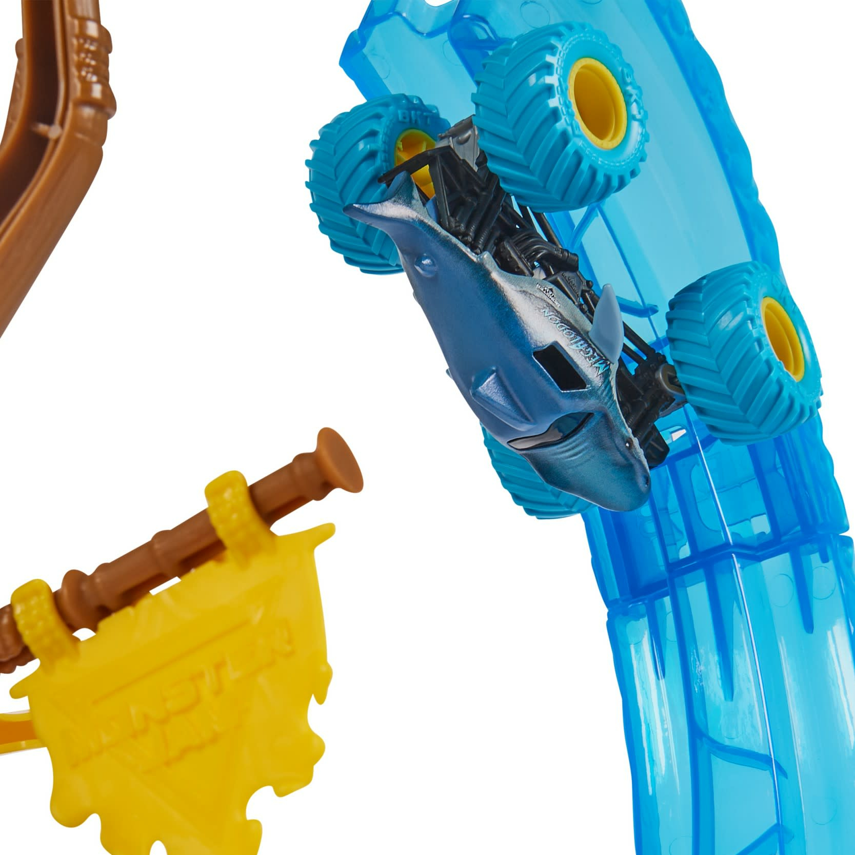 Ciężarówka potworna w kształcie rekina na niebieskim torze. Żółta flaga i brązowa konstrukcja z przodu.