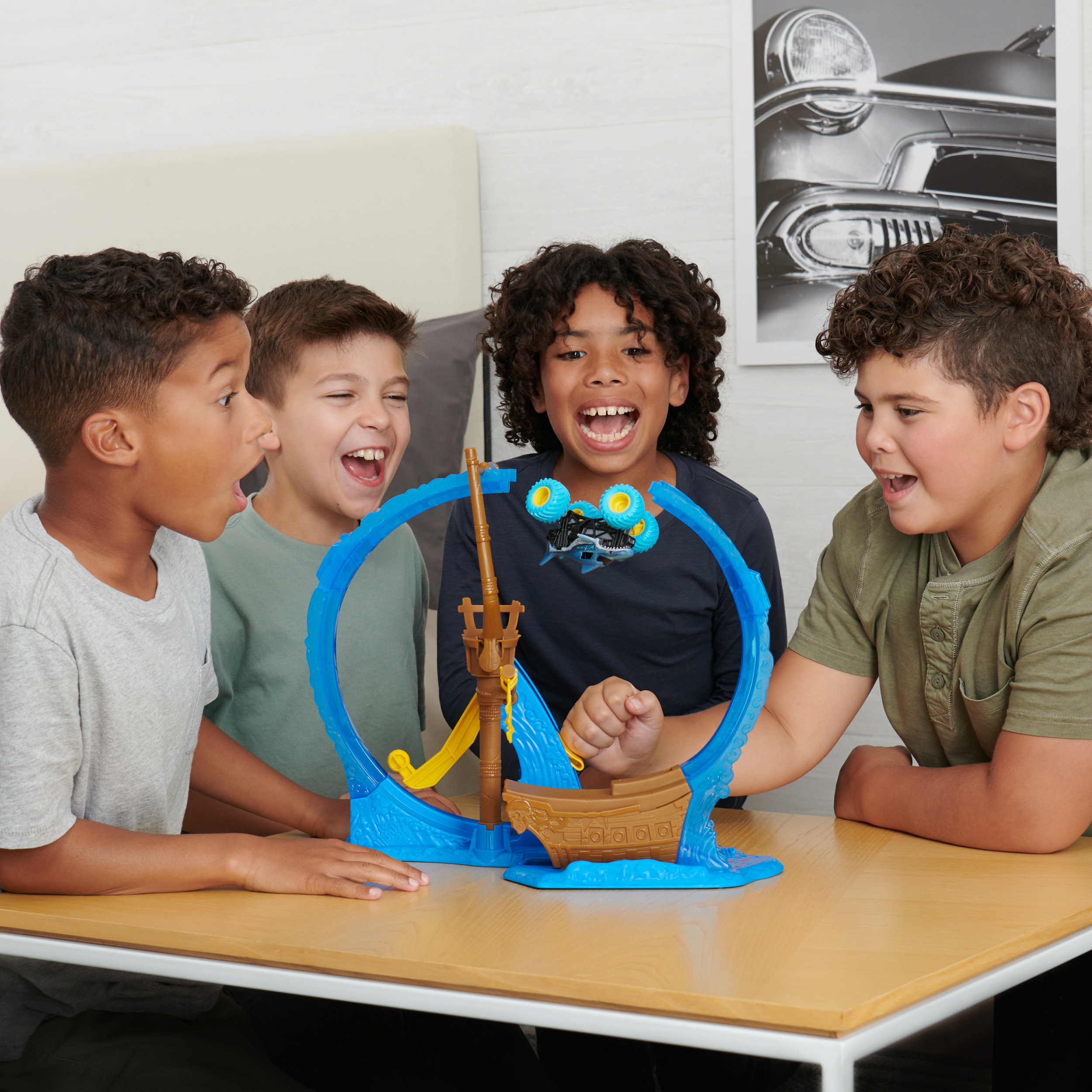 Czterech dzieci bawiących się torem samochodowym. Zabawkowa łódź i pętla znajdują się na środku niebieskiego toru.