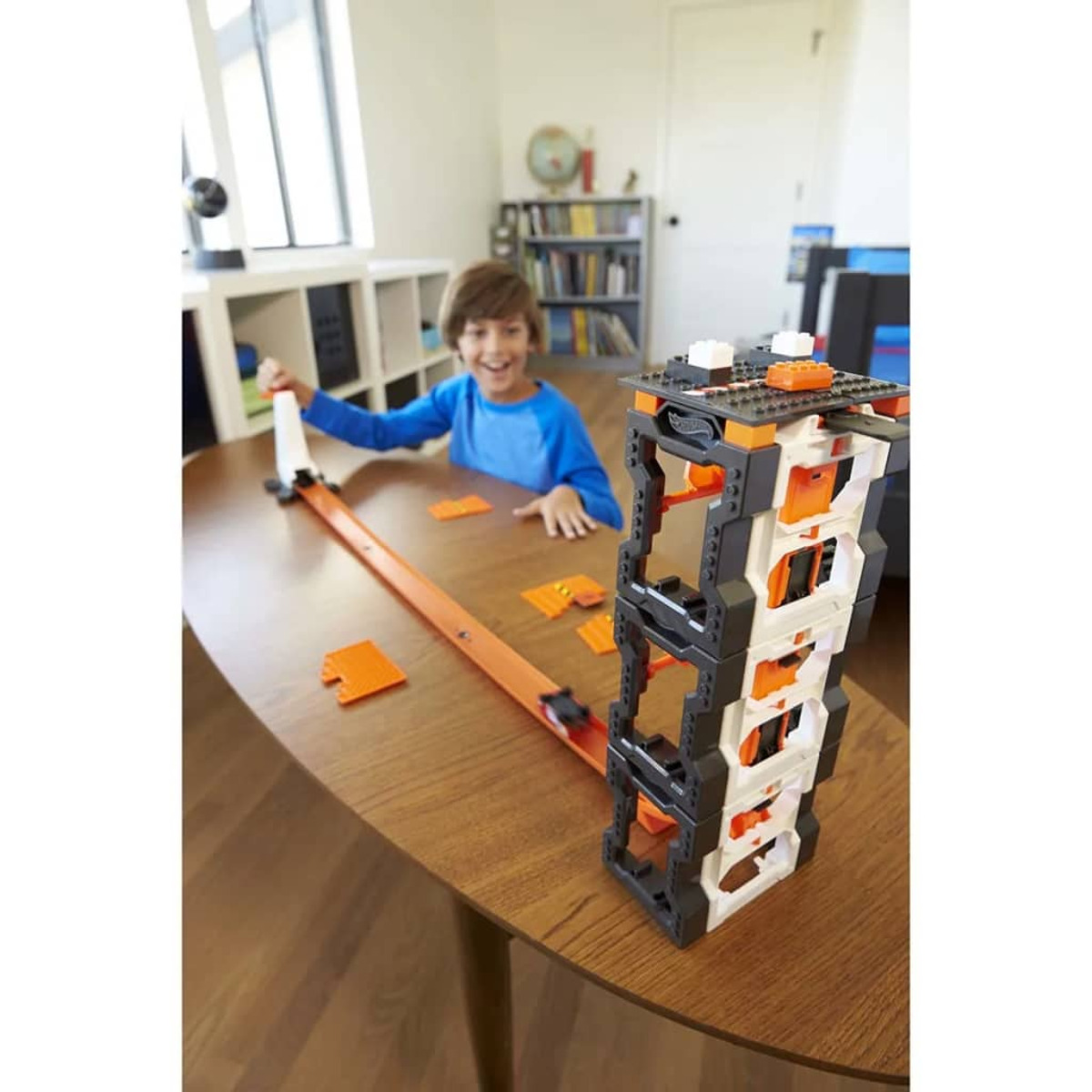 Chłopiec bawiący się torem wyścigowym. Tor jest pomarańczowy z wieżą i samochodem.