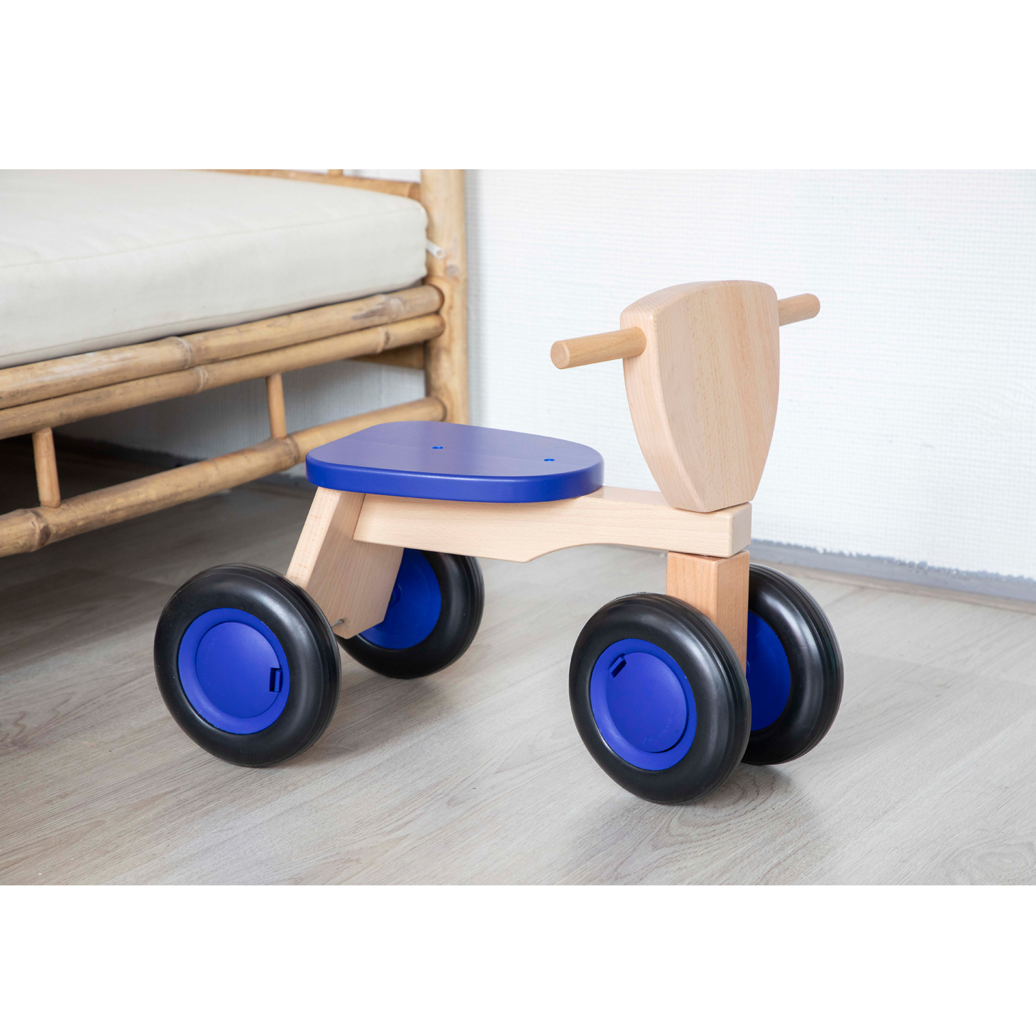 Ein Holzspielzeugfahrrad mit blauem Sitz und Reifen auf hellem Holzboden. Hintergrund ist ein Bambus.