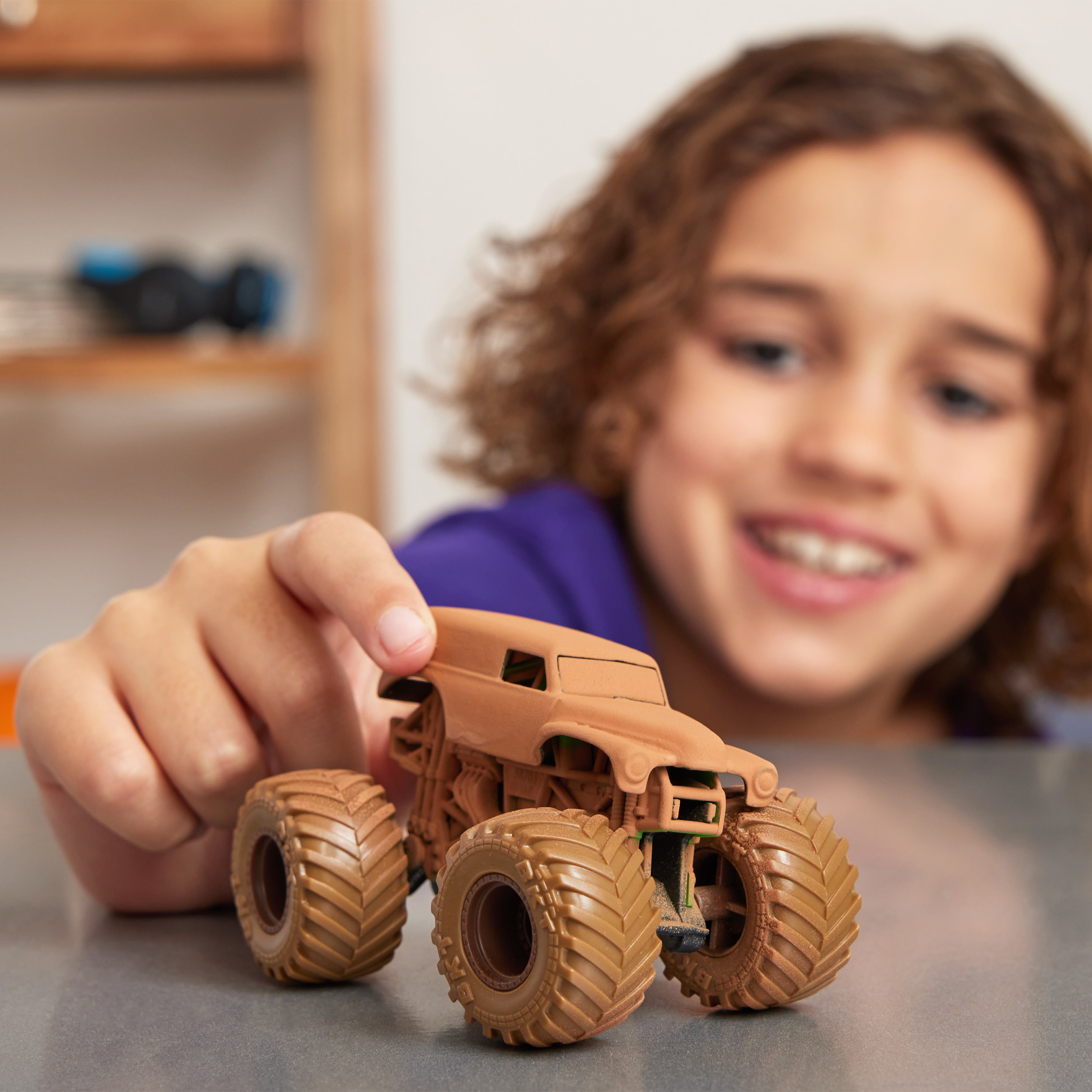 Dziecko uśmiecha się do zabawki monster truck w kolorze brązowym na szarej powierzchni.