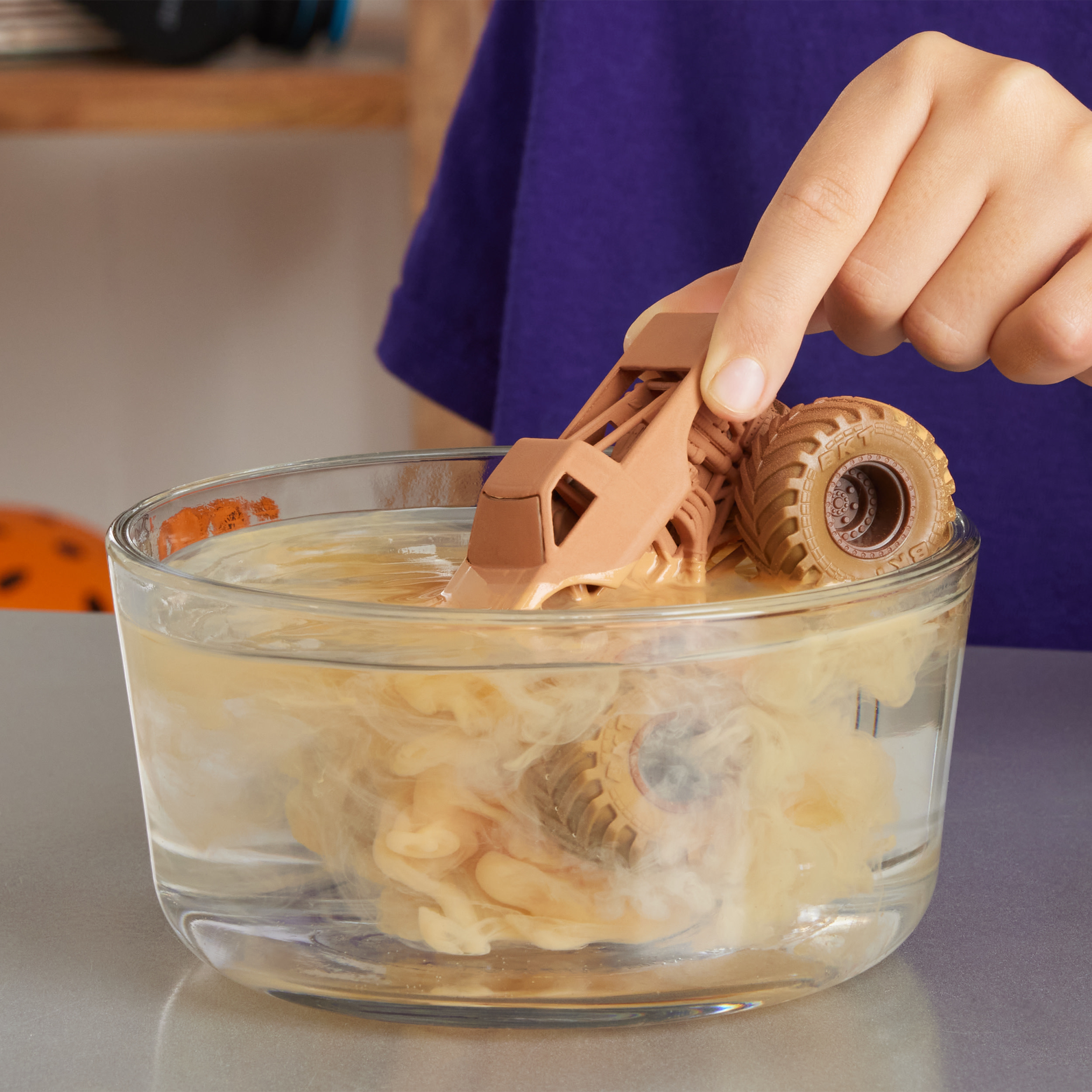 Zabawkowy monster truck jest zanurzony w mętnej wodzie. Ręka trzyma ciężarówkę.