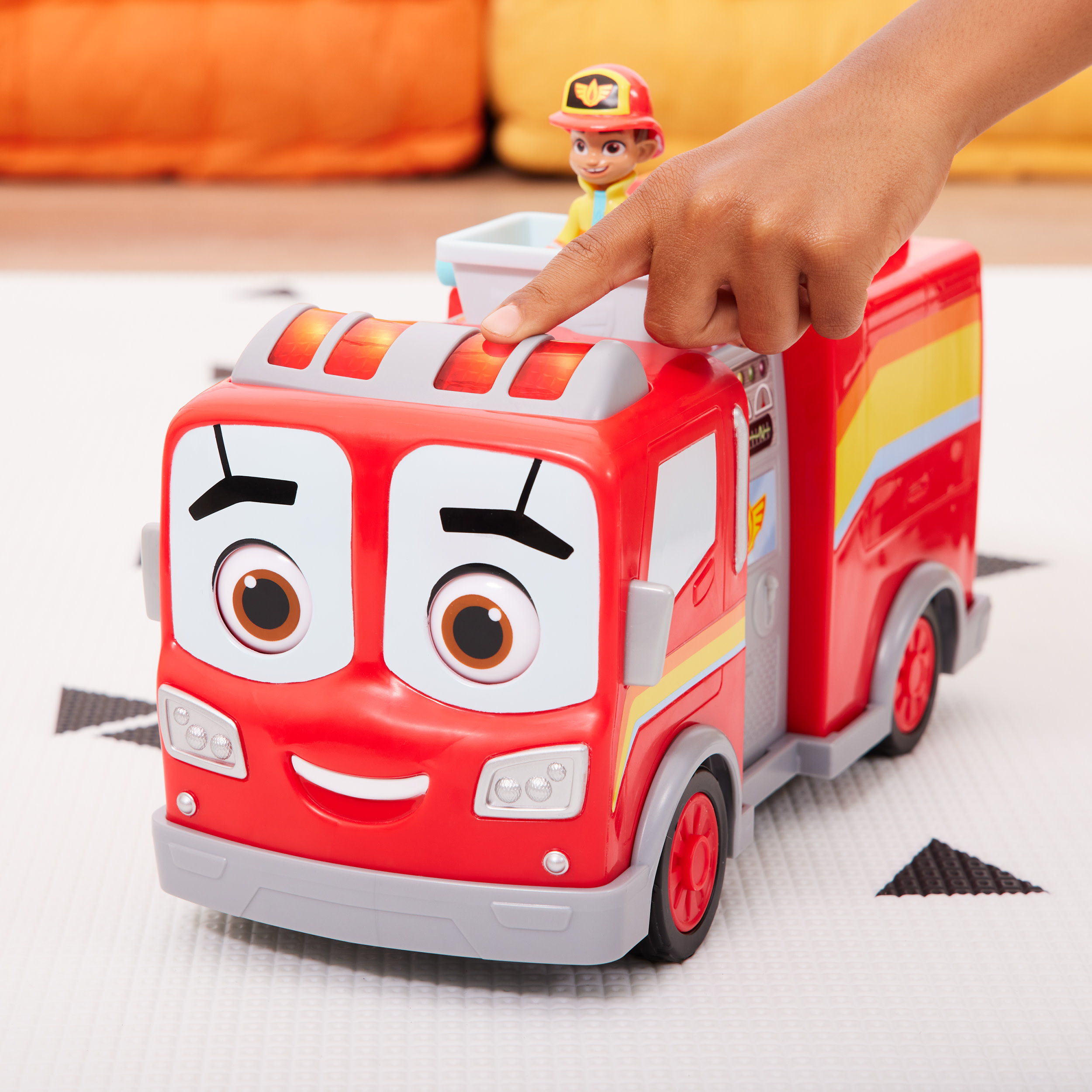Un camion dei pompieri rosso giocattolo con un viso sorridente e la mano di un bambino che preme un pulsante.