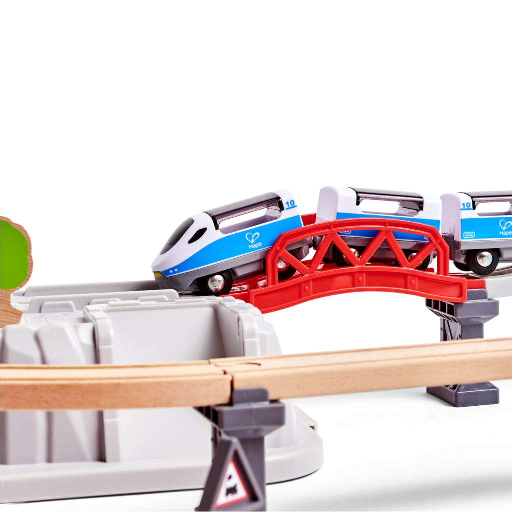 Zabawkowy pociąg na torze z mostem, drewnianym torem i szarymi podporami na białym tle.