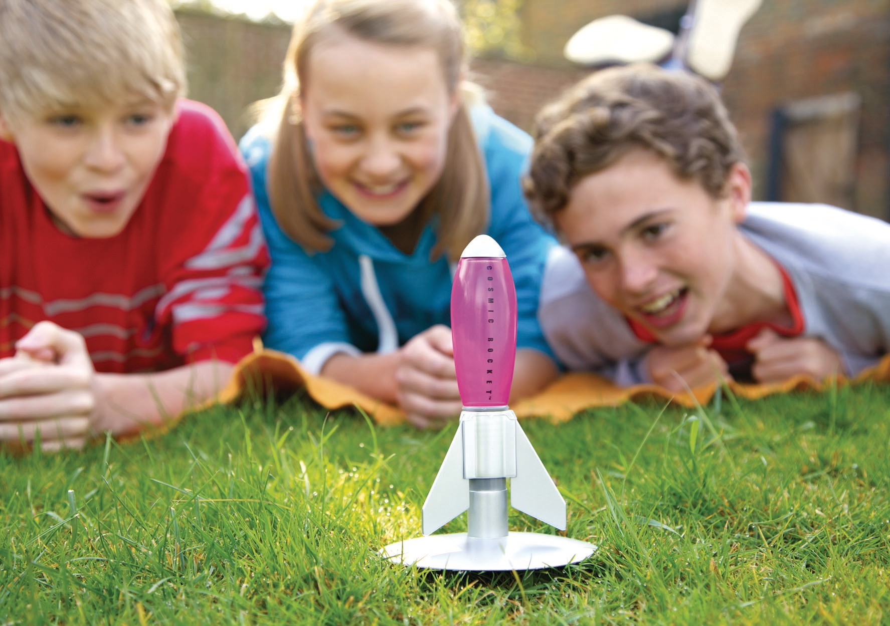 Trójka dzieci patrząca na zabawkową rakietę na trawie.