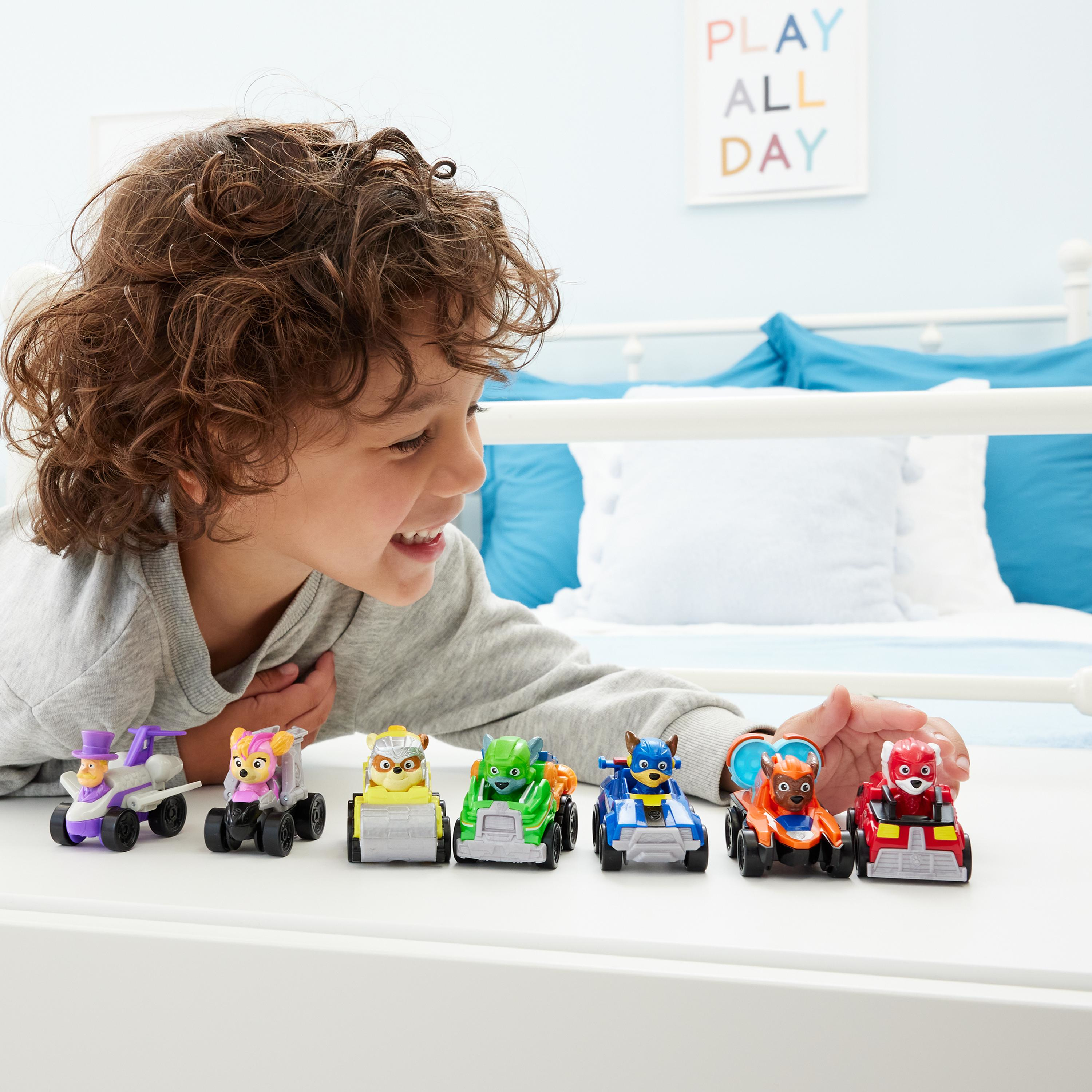 Un niño jugando con coches de juguete de Paw Patrol. Hay seis coches de juguete frente al niño.