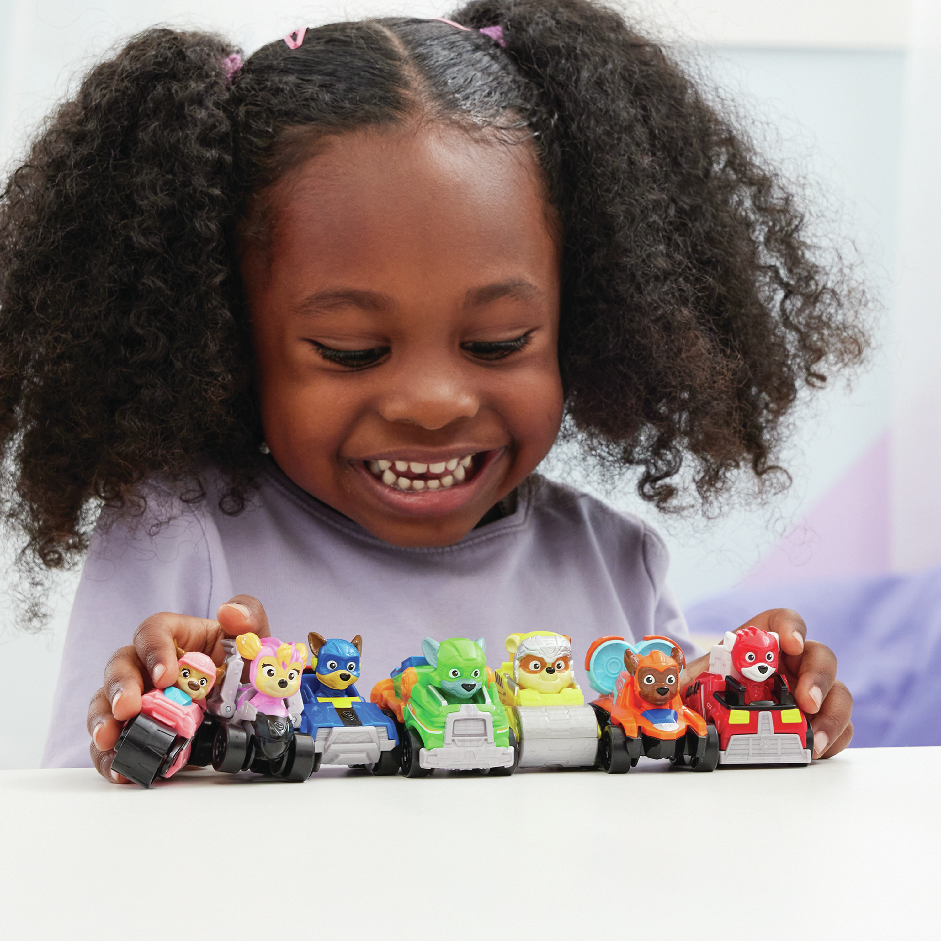 Un enfant souriant tenant des voitures jouets avec des personnages de Paw Patrol, sur fond clair.