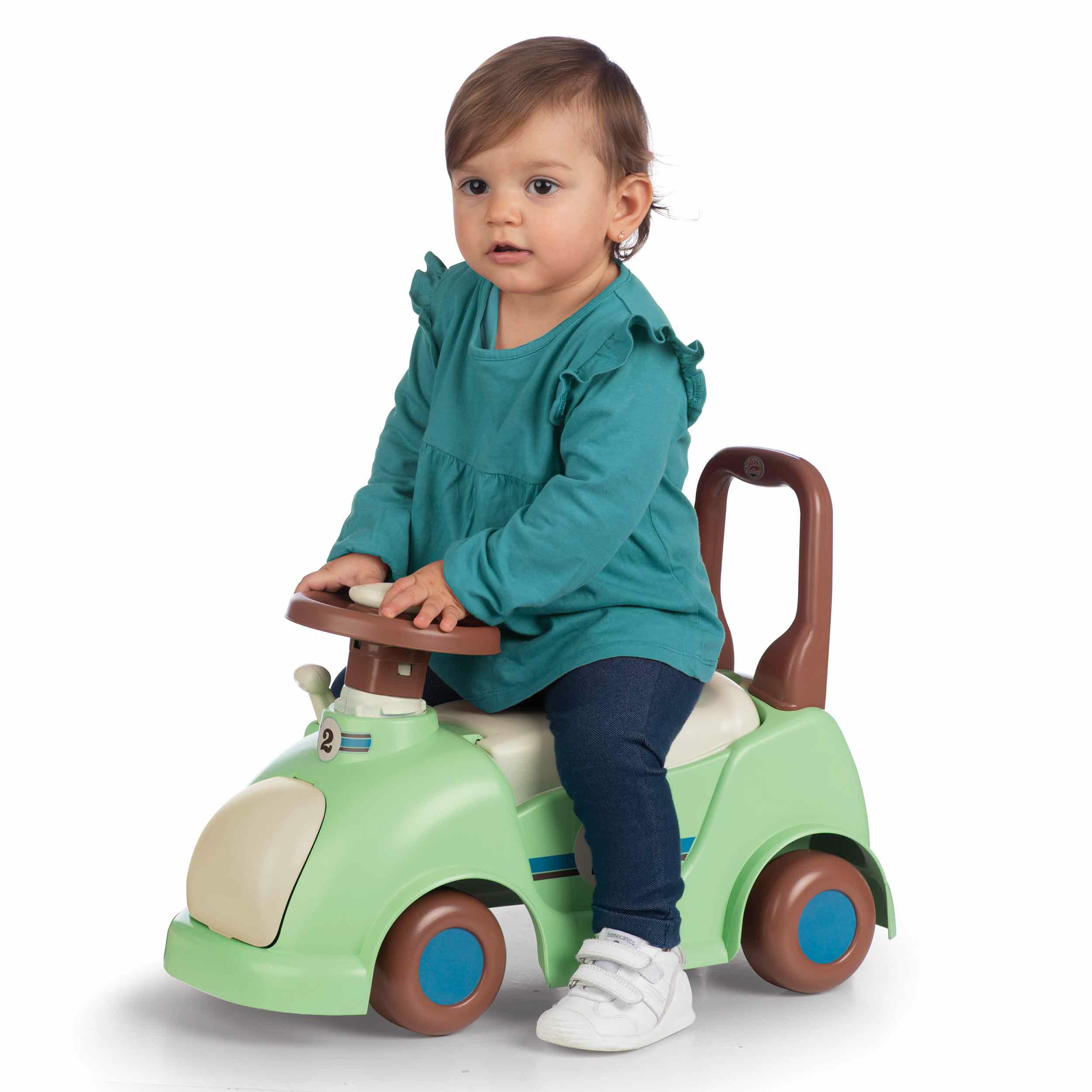 Bambino seduto su un'auto a spinta verde. Sfondo bianco.