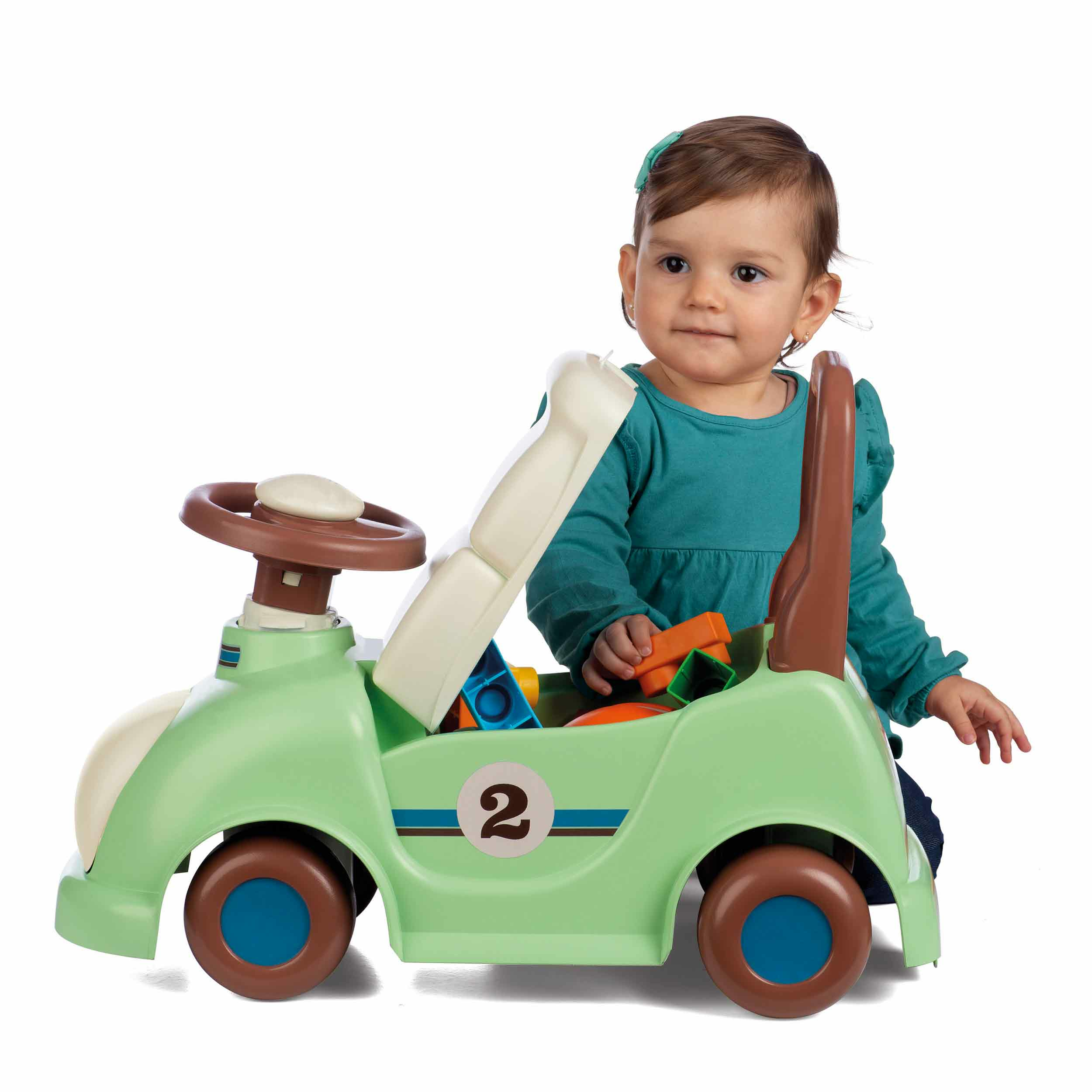 Un bambino è in un'auto a spinta verde con dei blocchi. Sfondo bianco.