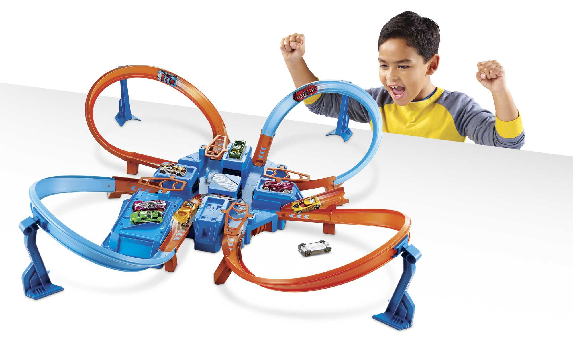 Junge jubelt in der Nähe einer Spielzeugstrecke mit Autos. Blaues und oranges Streckenset. Weißer Hintergrund.
