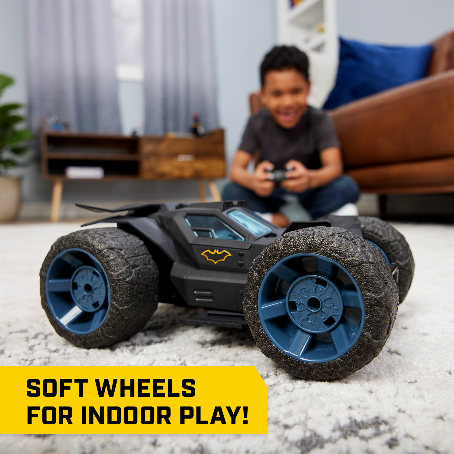 Un niño jugando con un coche de juguete negro con ruedas azules. Una pancarta amarilla dice 'SOFT WHEELS'.