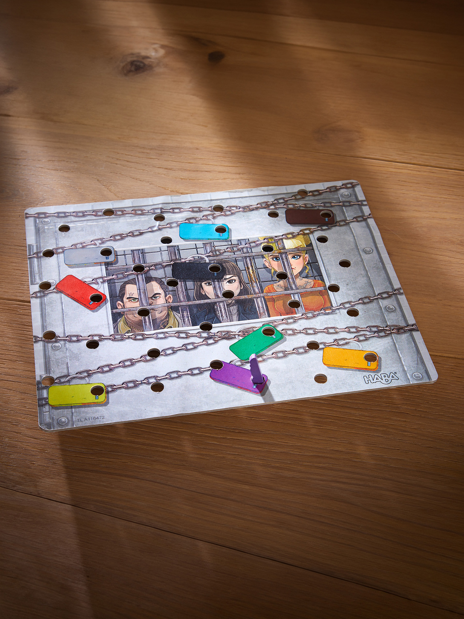 Ein Brettspiel mit Gefangenen hinter Gittern, farbigen Schlössern und Holzteilen.