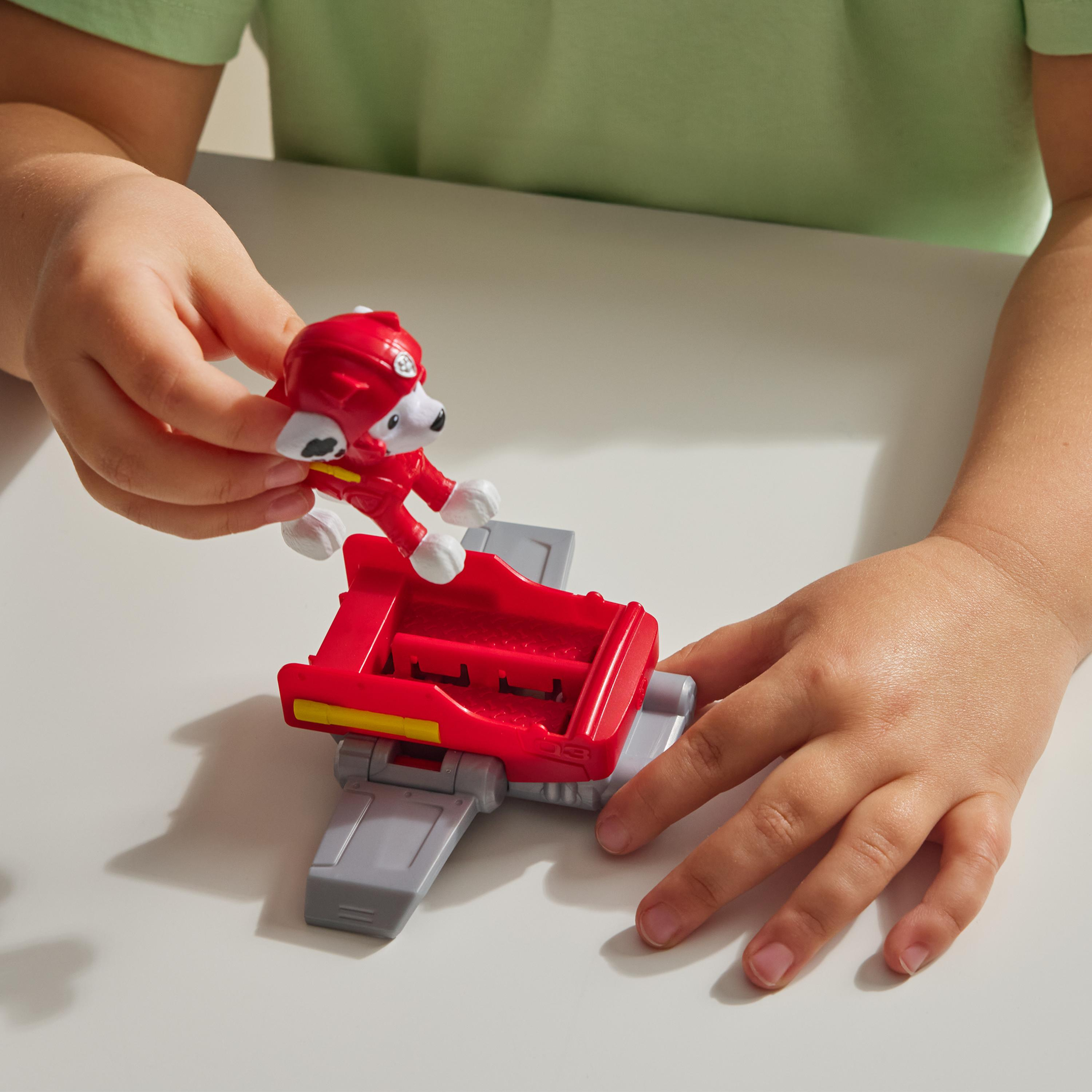 Ein Kind hält ein Paw Patrol Spielzeug. Marshall ist auf einem roten Fahrzeug, ein kleines graues Teil ist ebenfalls vorhanden.