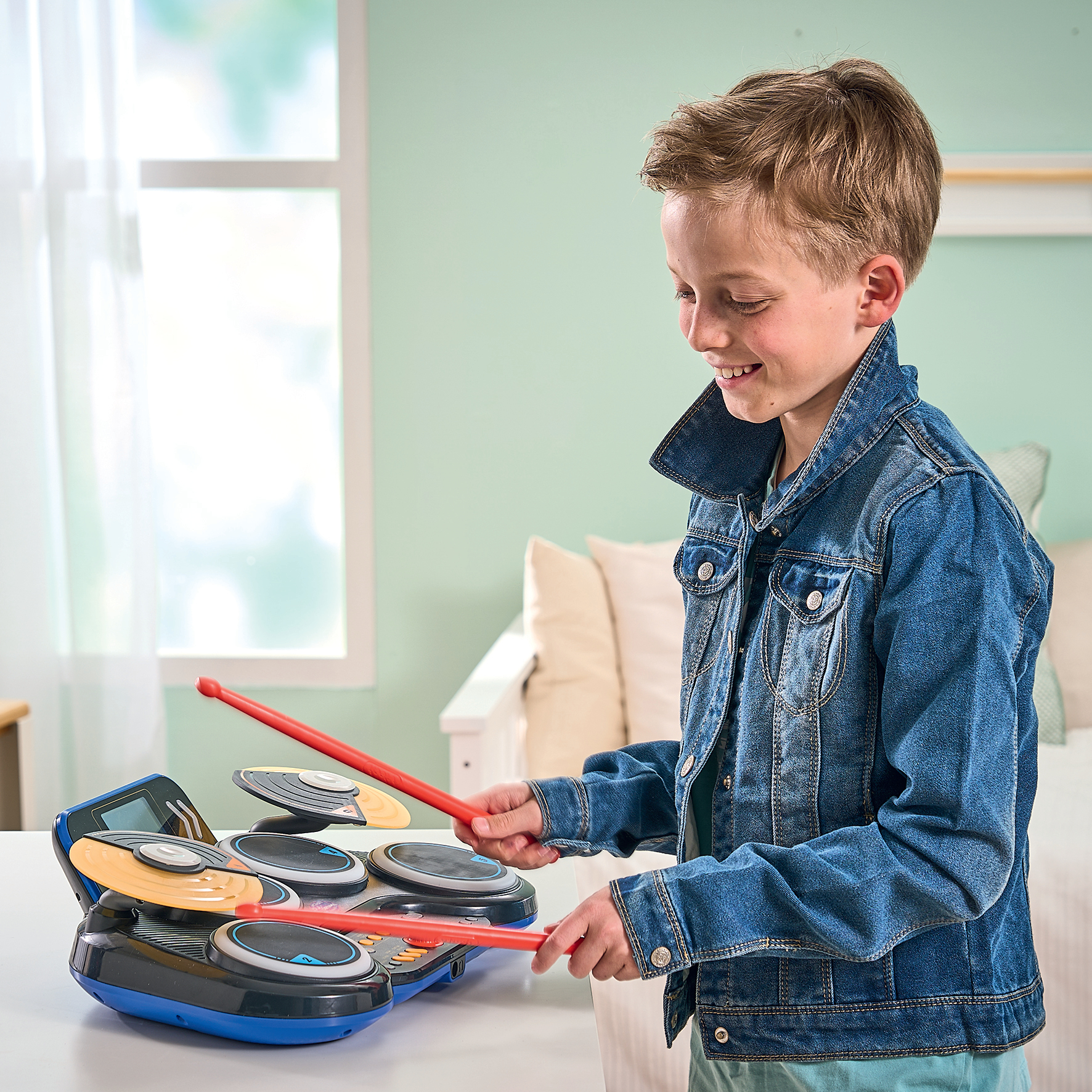 Ein Junge spielt ein Schlagzeug und trägt eine Jeansjacke. Rote Drumsticks werden gehalten.