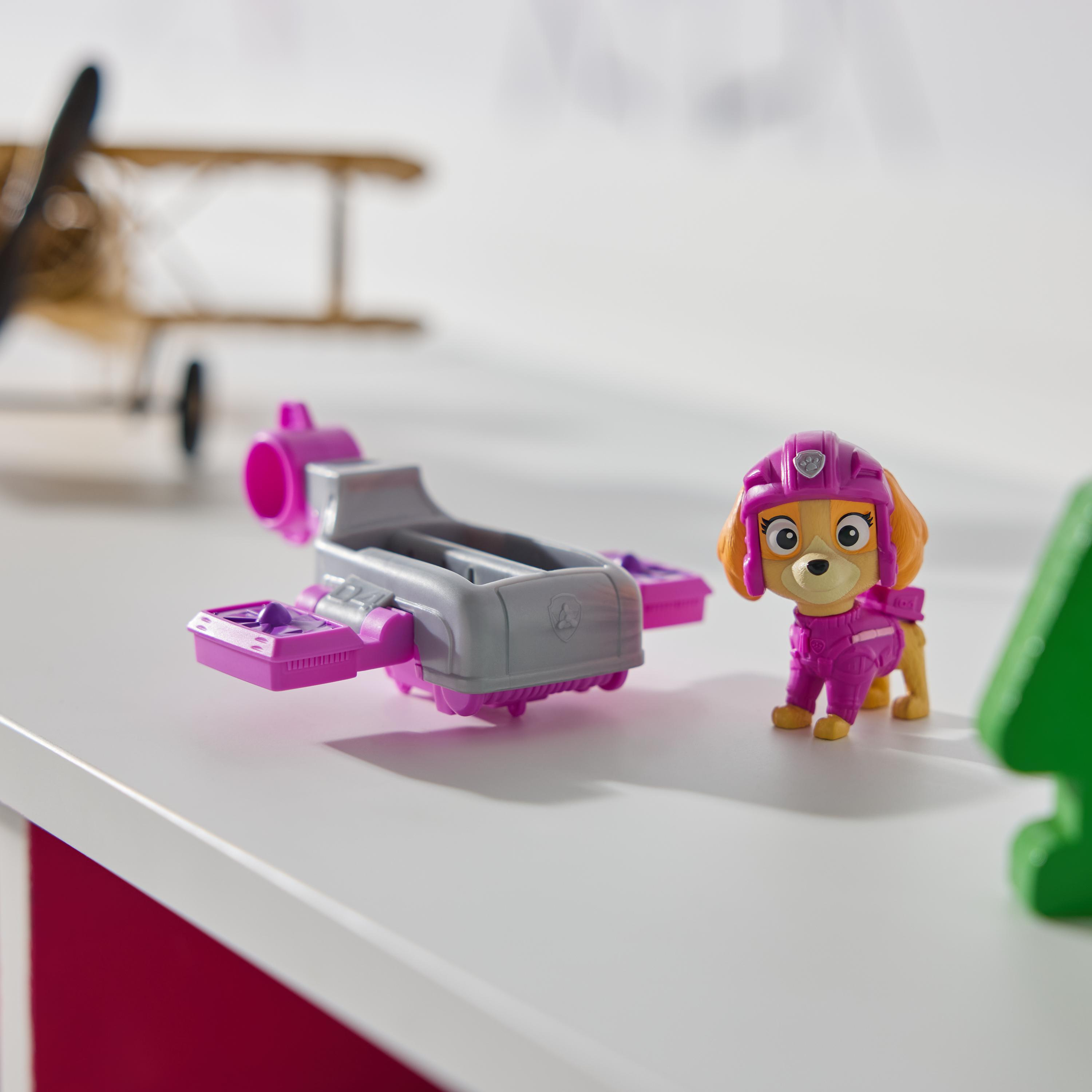 Skye-Spielzeug und Hoverboard auf weißer Oberfläche. Flugzeugmodell im Hintergrund. Grüne und weiße Elemente.