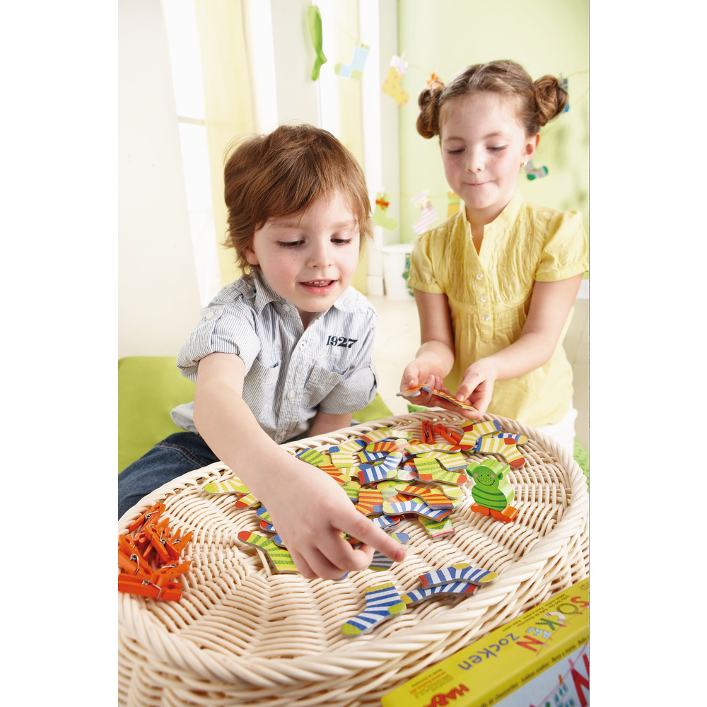 Zwei Kinder spielen mit einem Puzzlespiel in einem Weidenkorb auf einem hellen Holztisch. Einige Wäscheklammern.