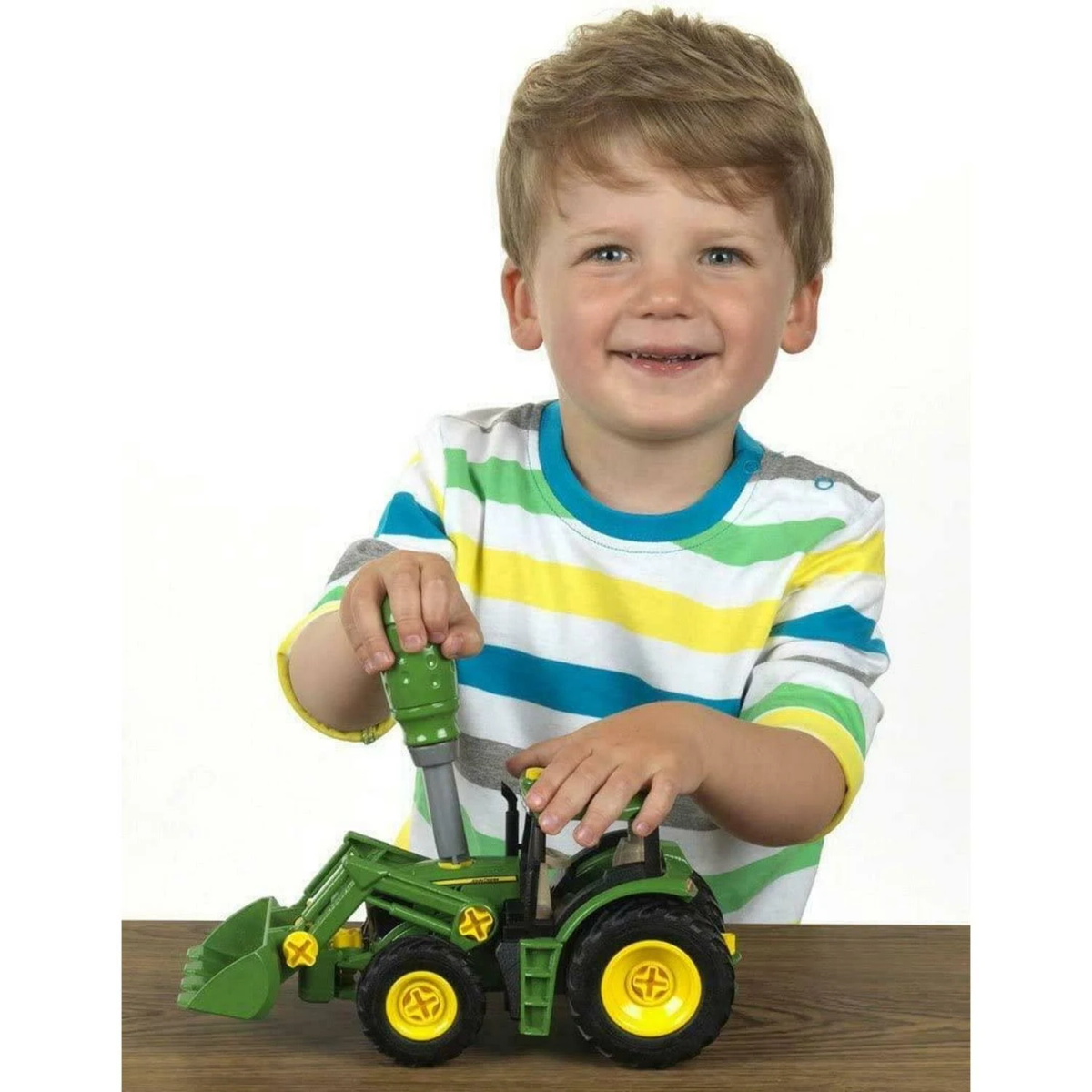 Mały chłopiec bawi się zielono-żółtą zabawką w postaci traktora. Traktor ma ładowacz czołowy.