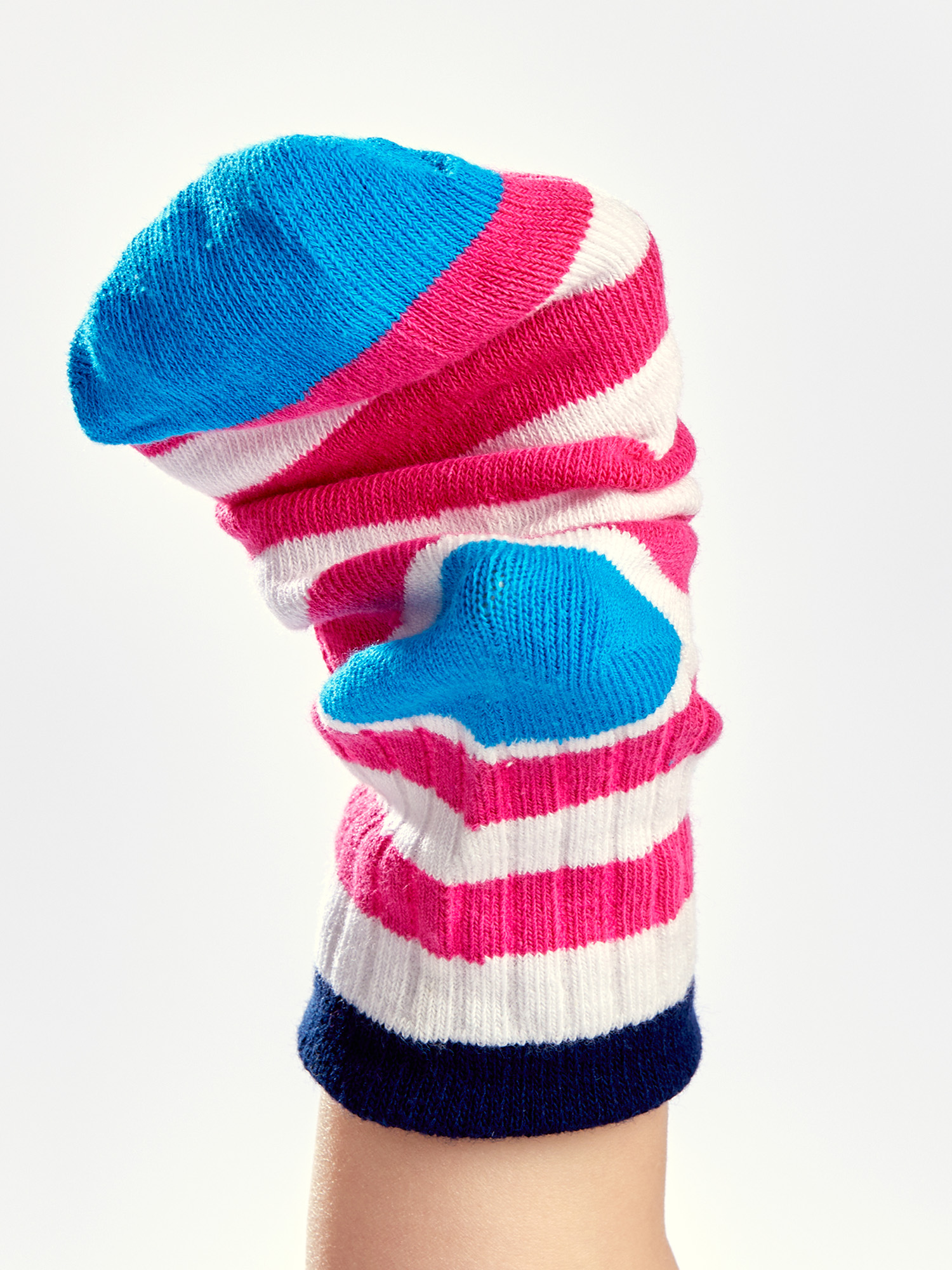 Eine Hand mit einer gestreiften Socke. Die Socke ist blau, pink, weiß und marineblau. Der Hintergrund ist weiß.