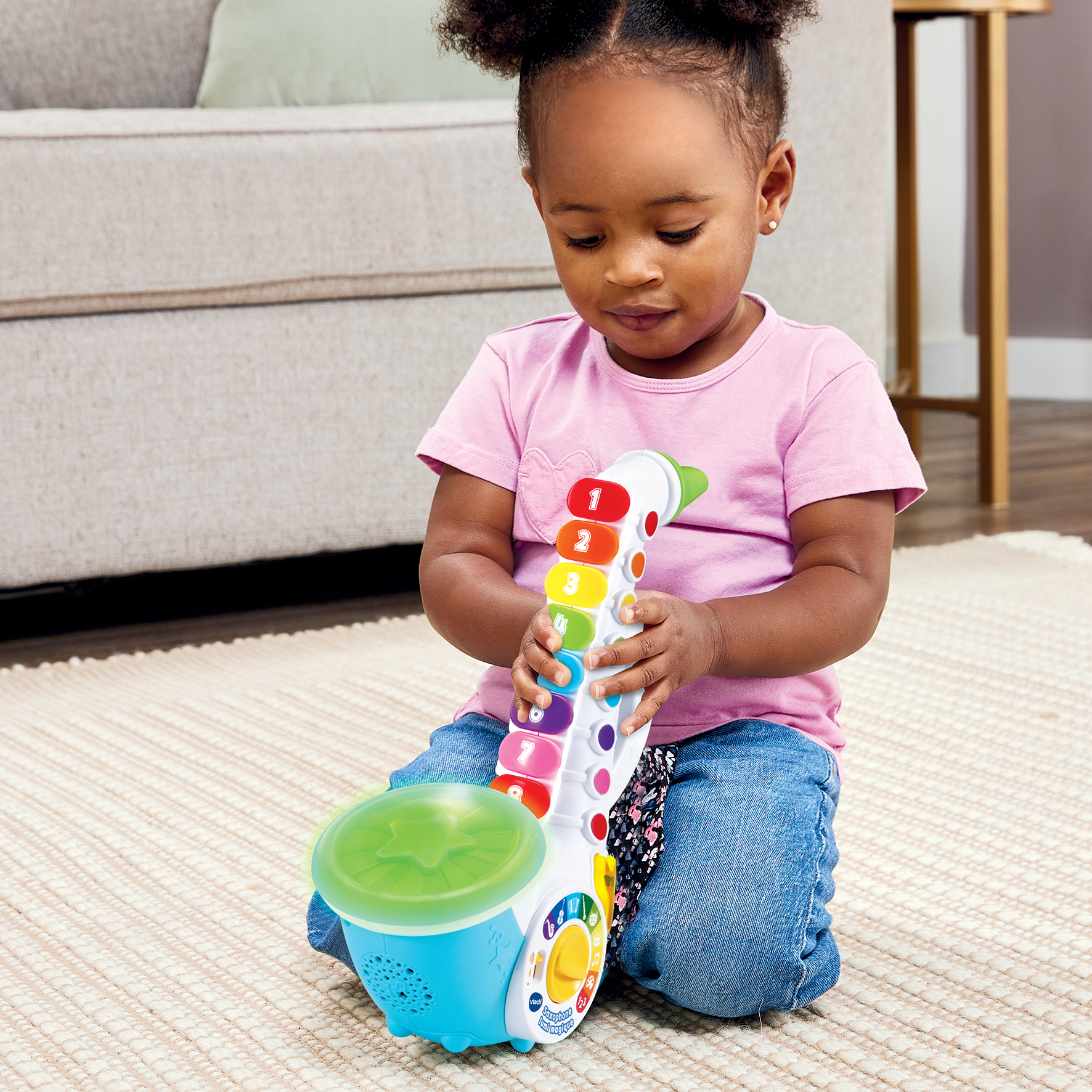 Una niña está sentada y jugando con un saxofón de juguete. El saxofón tiene botones coloridos.
