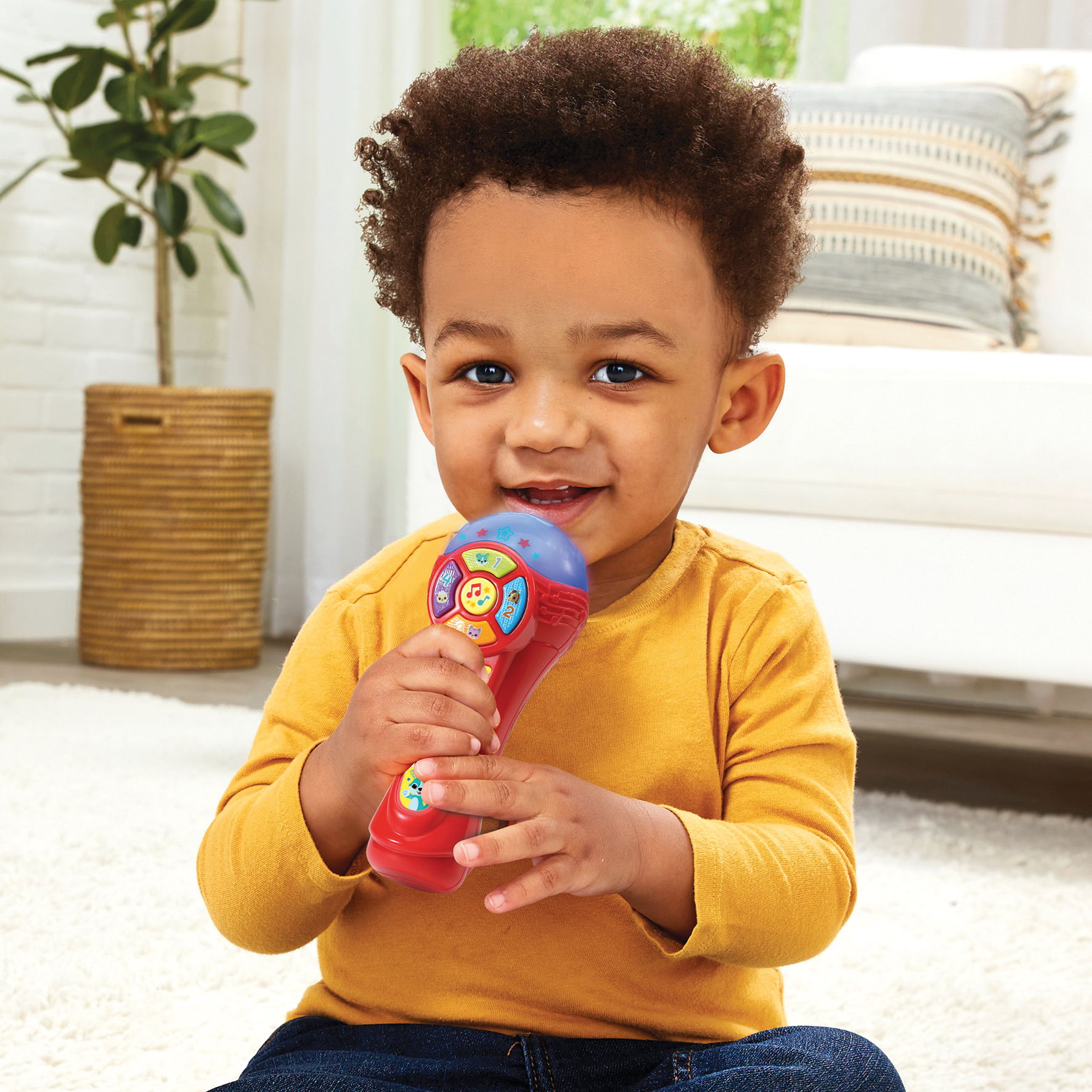 Un niño pequeño sosteniendo un micrófono de juguete rojo y azul, sonriendo a la cámara.