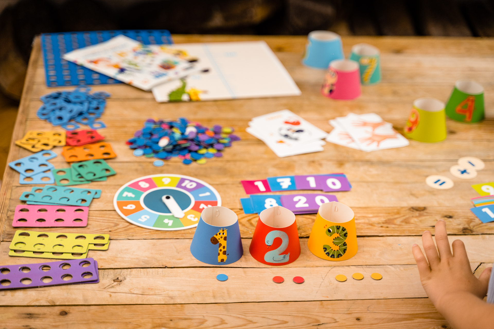 Stół pokryty jest kolorowymi elementami zabawek, w tym kubkami, kartami i drewnianymi elementami gier.