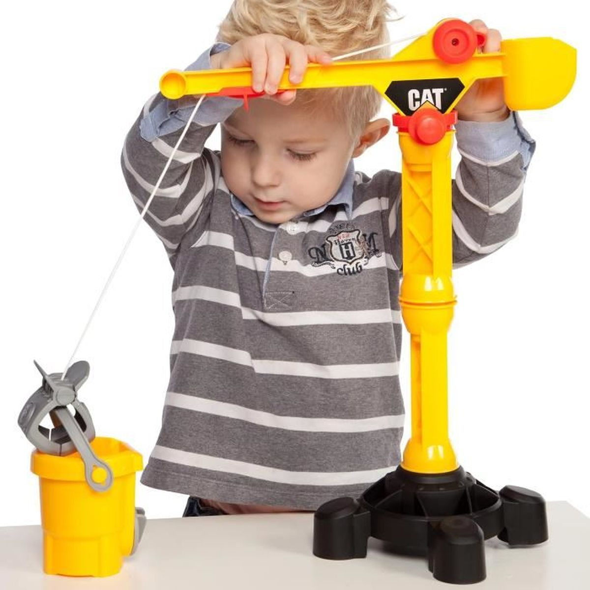 Dziecko używa żółtego dźwigu CAT z wiadrem, dźwig na stole w pokoju.